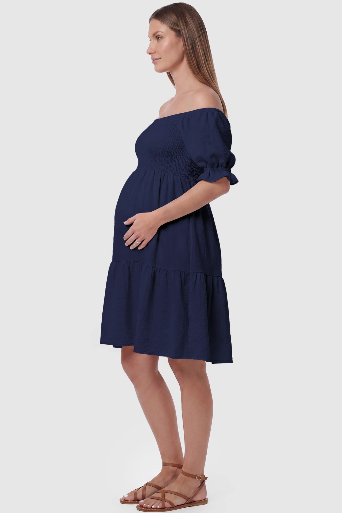 Smocked Off-Shoulder Empire Waist Maternity Short Dress Smocked off-shoulder empire waist maternity short dress in navy blue with bump-friendly empire waist fit, side view on pregnant model