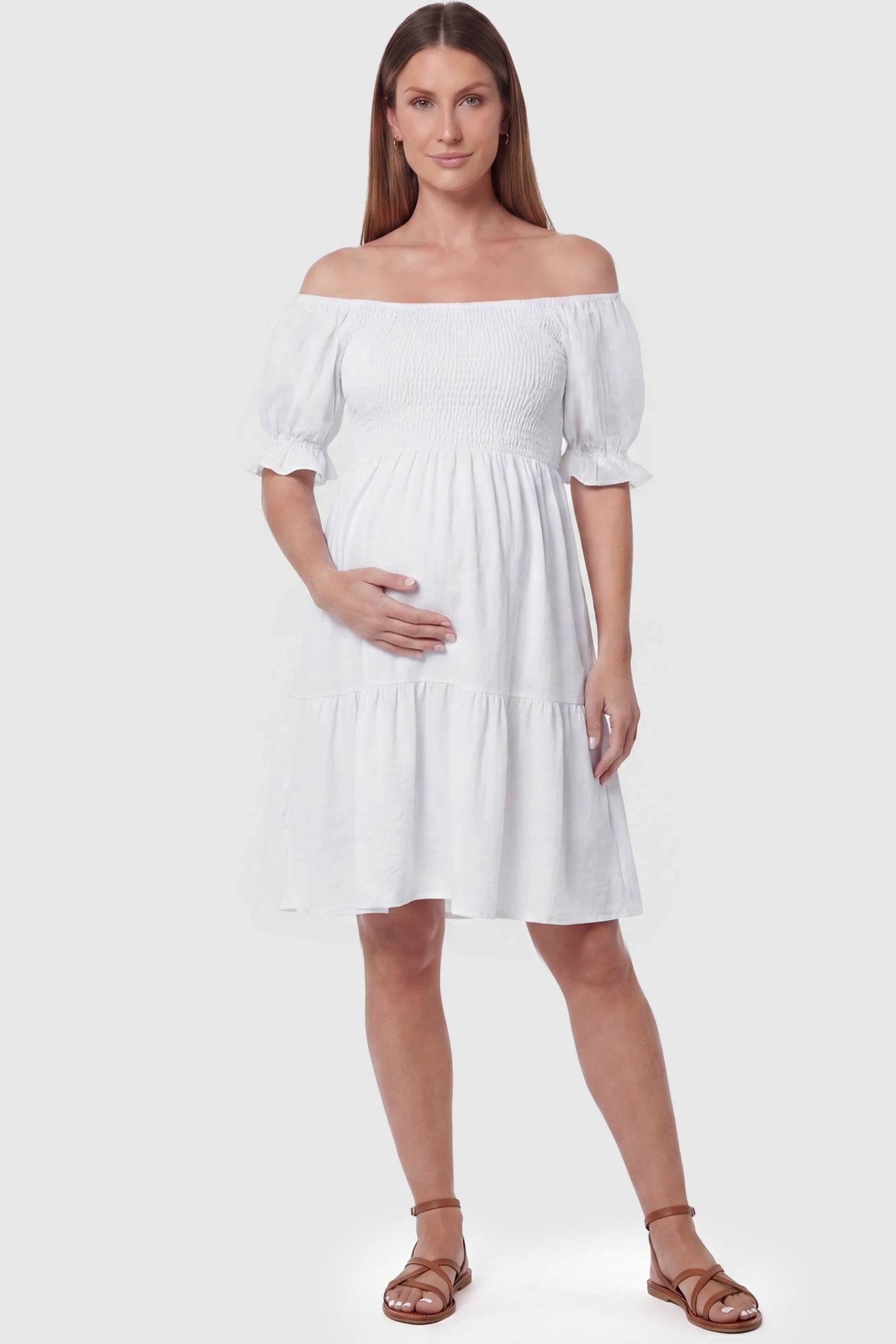 Smocked Off-Shoulder Empire Waist Maternity Short Dress Smocked off-shoulder empire waist maternity short dress in white with smocked bodice detail, front view on pregnant model
