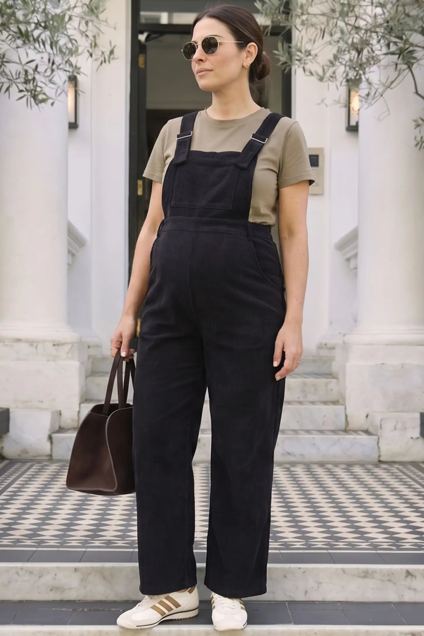 Corduroy Wide Leg Maternity Jumpsuit Corduroy Wide-Leg Maternity Jumpsuit in Black featuring a relaxed wide-leg silhouette on a pregnant woman in outdoor setting, front view.