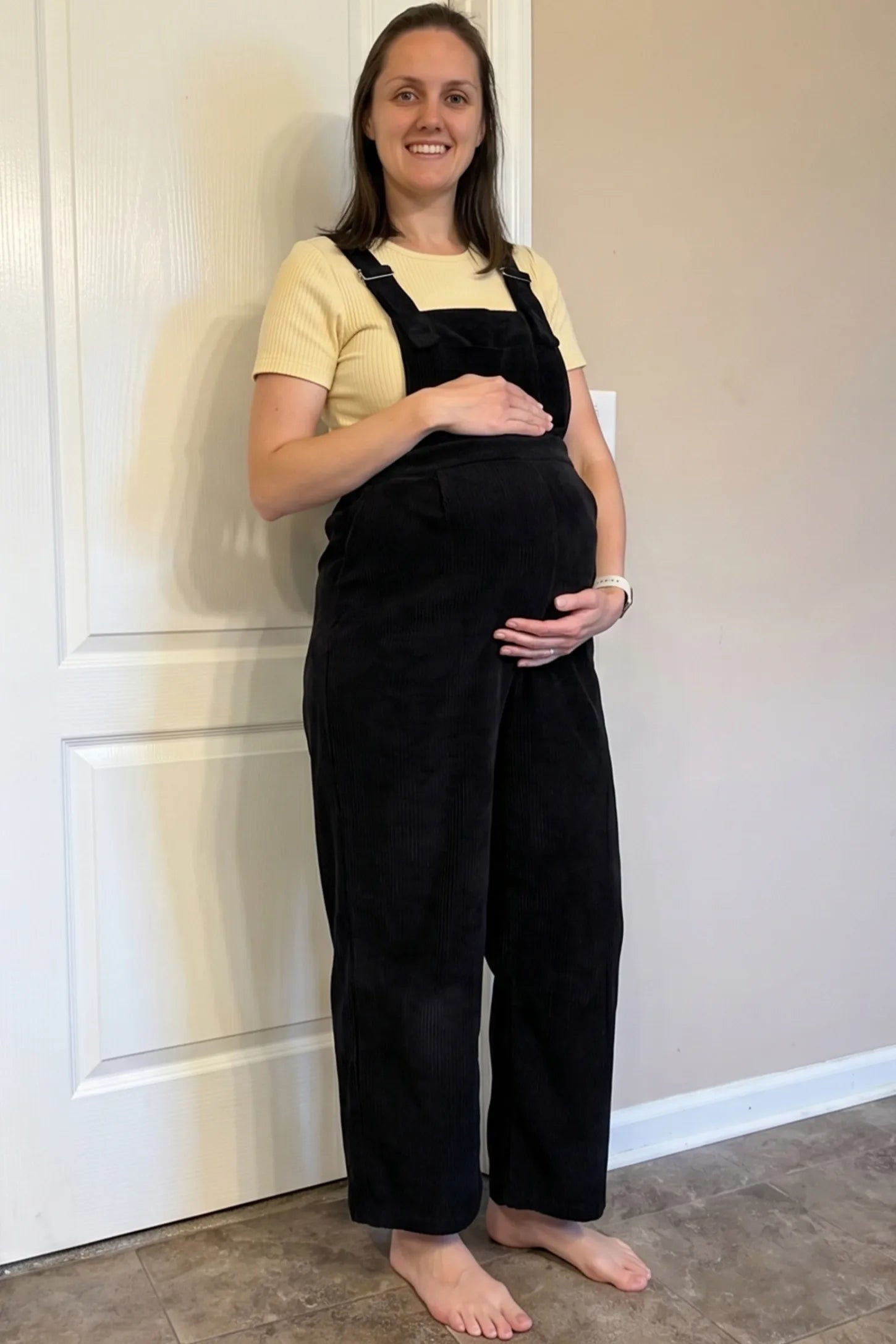 Corduroy Wide Leg Maternity Jumpsuit Corduroy Wide-Leg Maternity Jumpsuit in Black featuring a relaxed wide-leg silhouette on a pregnant woman in indoor setting, front view.