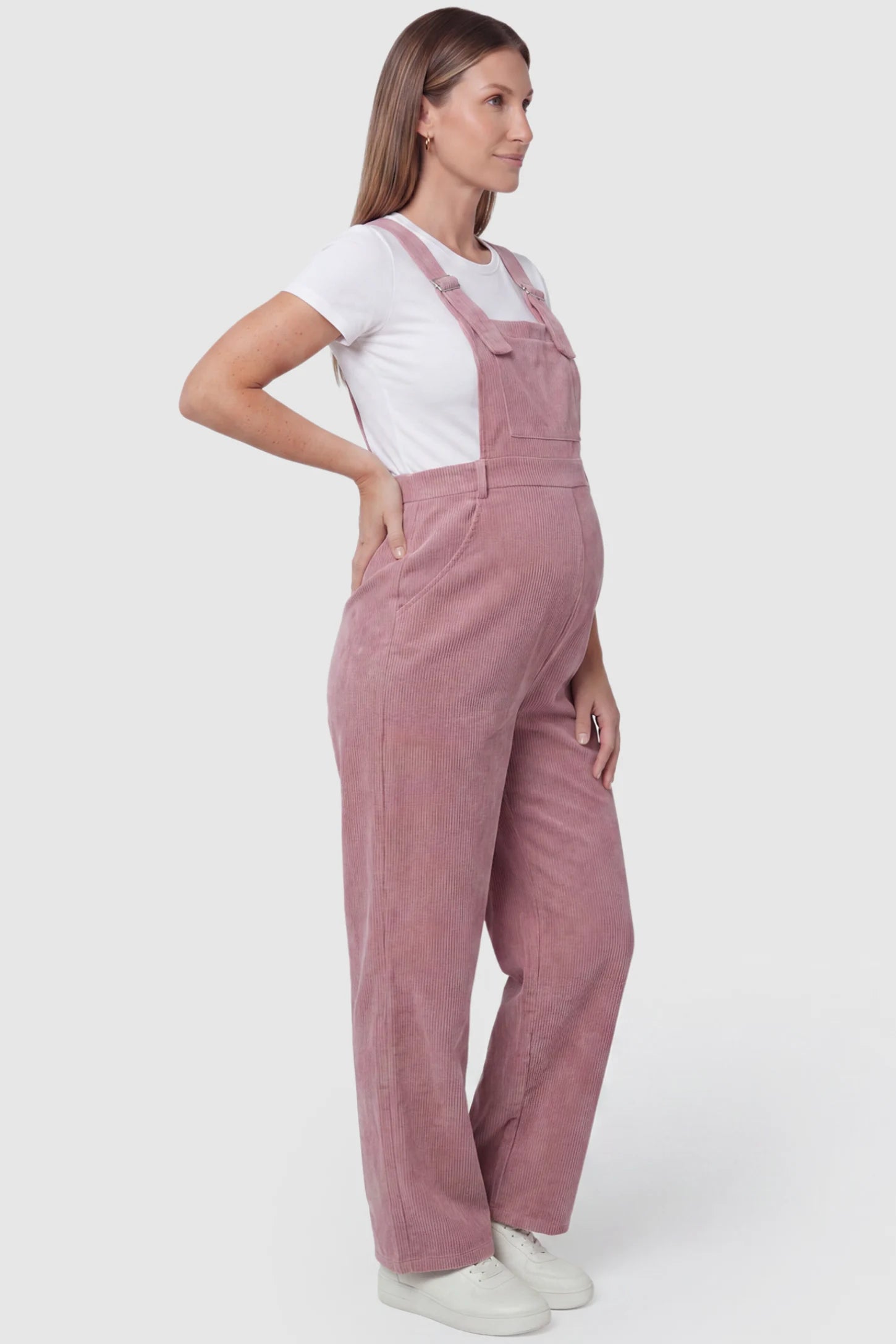 Corduroy Wide Leg Maternity Jumpsuit Corduroy Wide-Leg Maternity Jumpsuit in Pink featuring a relaxed wide-leg silhouette on a pregnant model, side view.