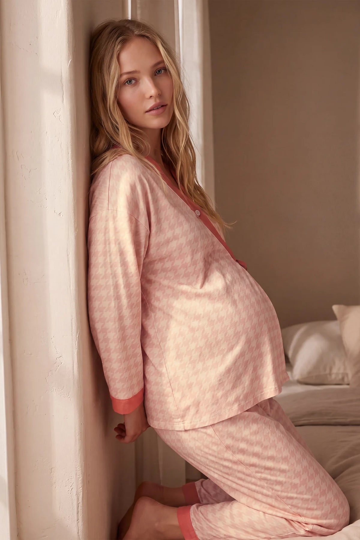 Cotton Houndstooth Nursing Pajama Set Cotton Houndstooth Nursing Pajama Set in Pink Houndstooth featuring flexible stretch fit, long sleeves, and contrast lapel trim on a pregnant model, indoor standing view.