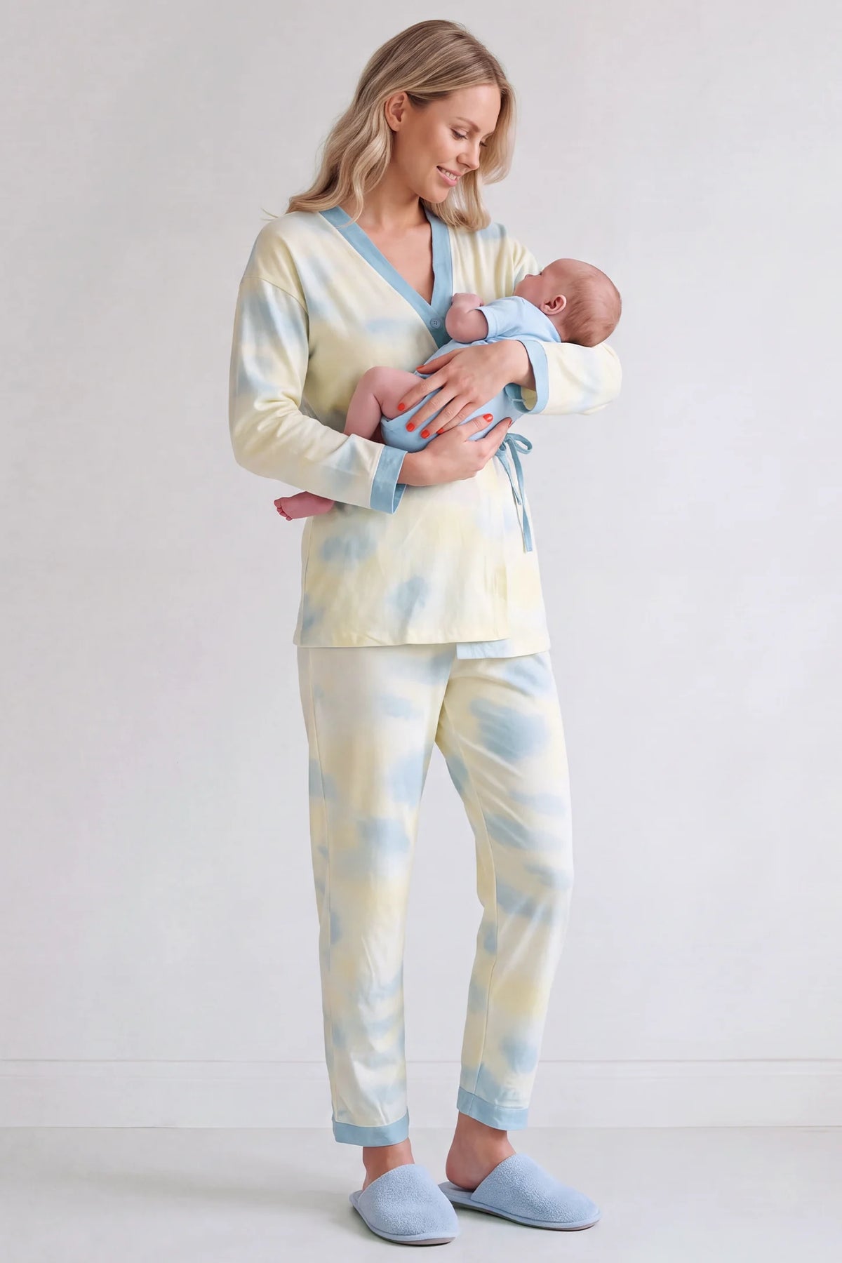 Cotton Tie-Dye Maternity & Nursing Pajama Set Cotton Tie-Dye Maternity & Nursing Pajama Set in Blue Tie-Dye featuring postpartum nursing access, soft cotton-rich feel, and full pajama set on a mother cradling her newborn baby, standing front view.