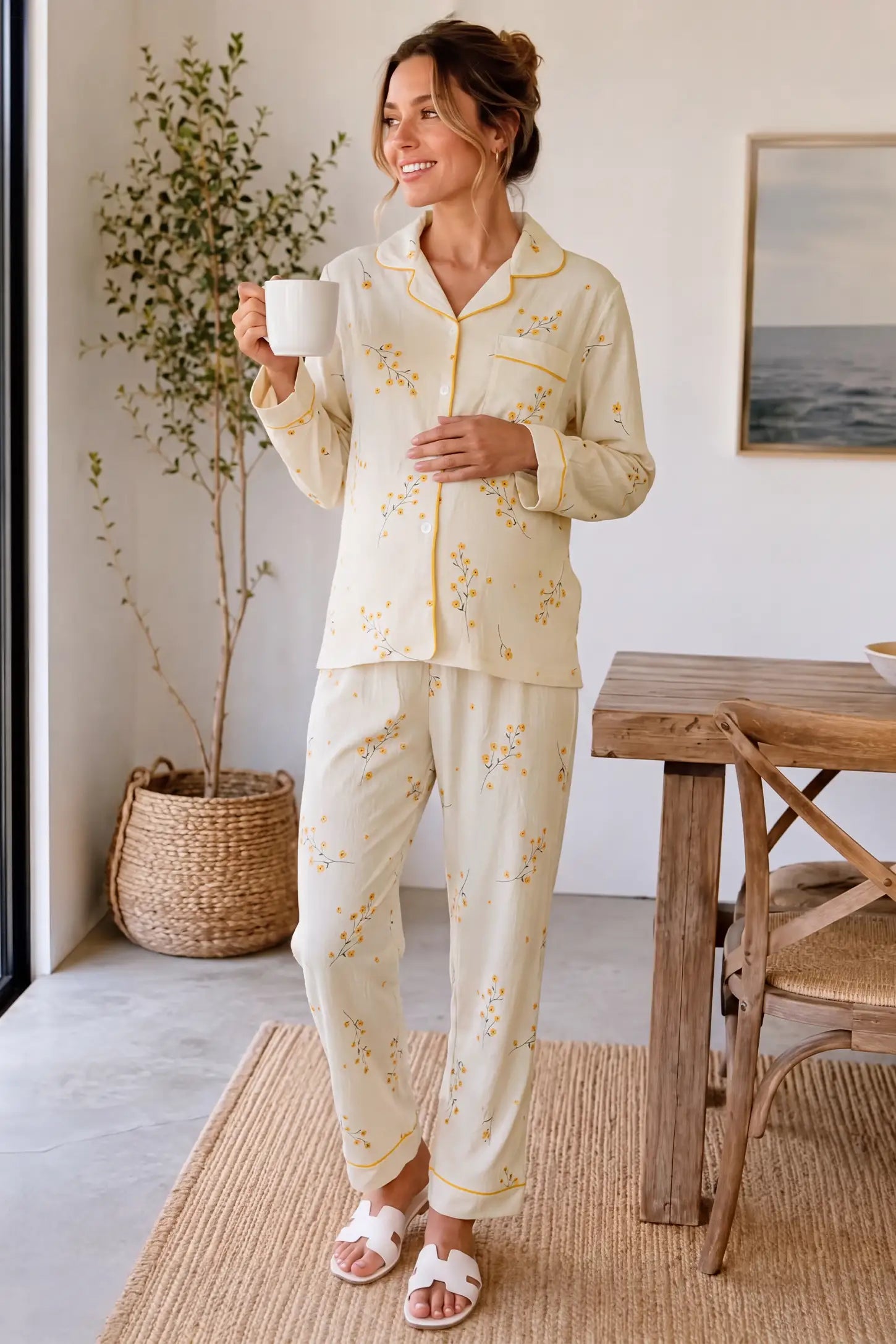 Cozy Floral Cotton Maternity Pajama Set Cozy Floral Cotton Maternity Pajama Set in Yellow Daisy featuring countryside charm yellow floral print, long sleeves, and a relaxed fit on a pregnant model holding a cup, home interior standing view.