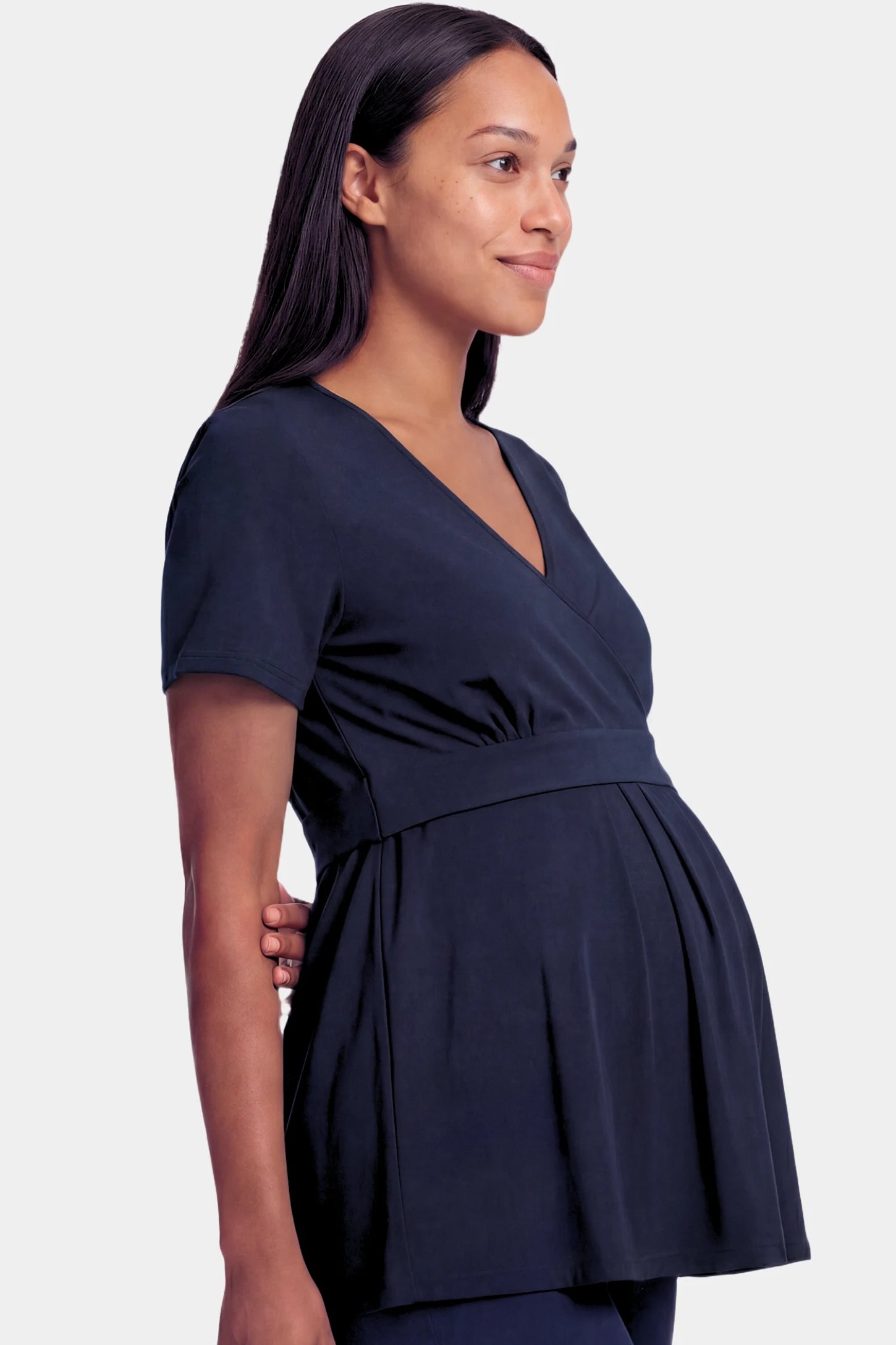 Crossover Short Sleeve Maternity & Nursing Top Crossover Short Sleeve Maternity & Nursing Top in dark blue featuring a crossover V-neck and empire waist on a pregnant model.
