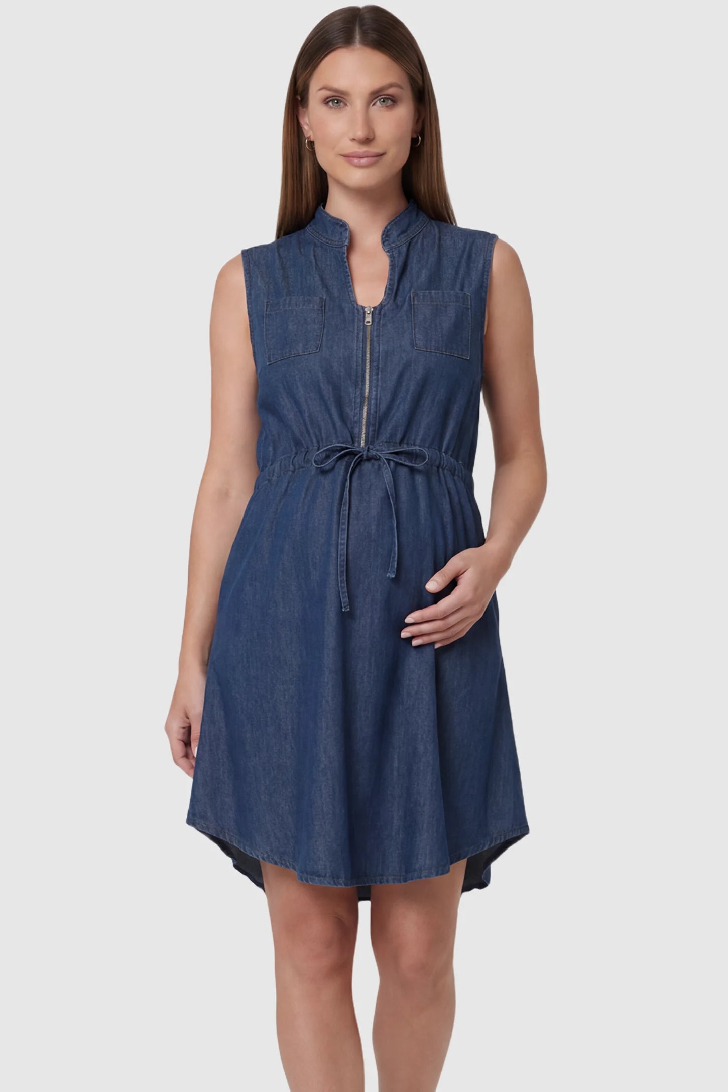 Denim Sleeveless Maternity & Nursing Midi Shirt Dress in dark blue featuring front zipper, stand collar, and adjustable drawstring waist on a pregnant model showing front.