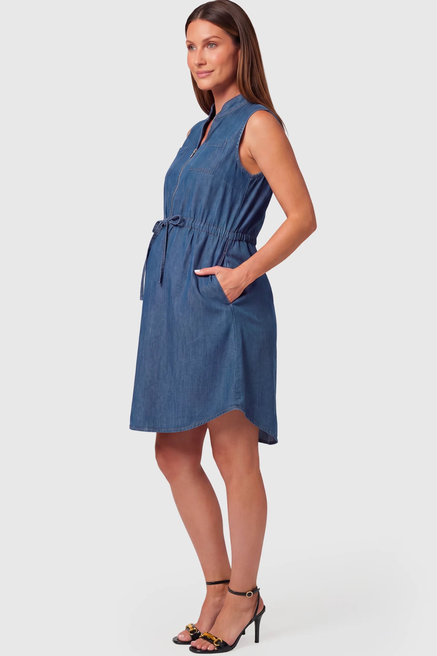 Denim Sleeveless Maternity & Nursing Midi Shirt Dress in dark blue featuring front zipper, stand collar, and adjustable drawstring waist on a pregnant model.