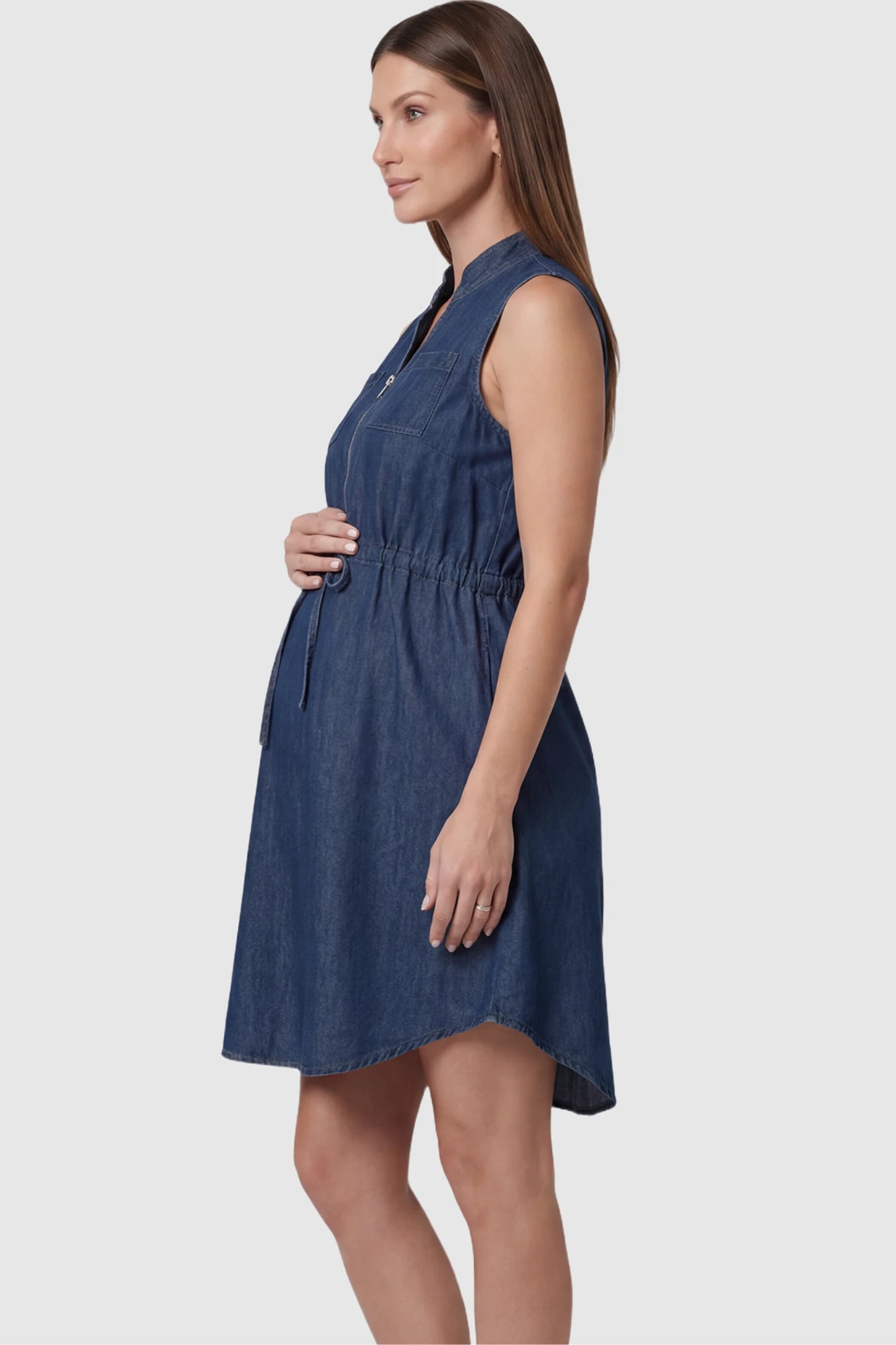 Denim Sleeveless Maternity & Nursing Midi Shirt Dress in dark blue featuring front zipper, stand collar, and adjustable drawstring waist on a pregnant model showing side.