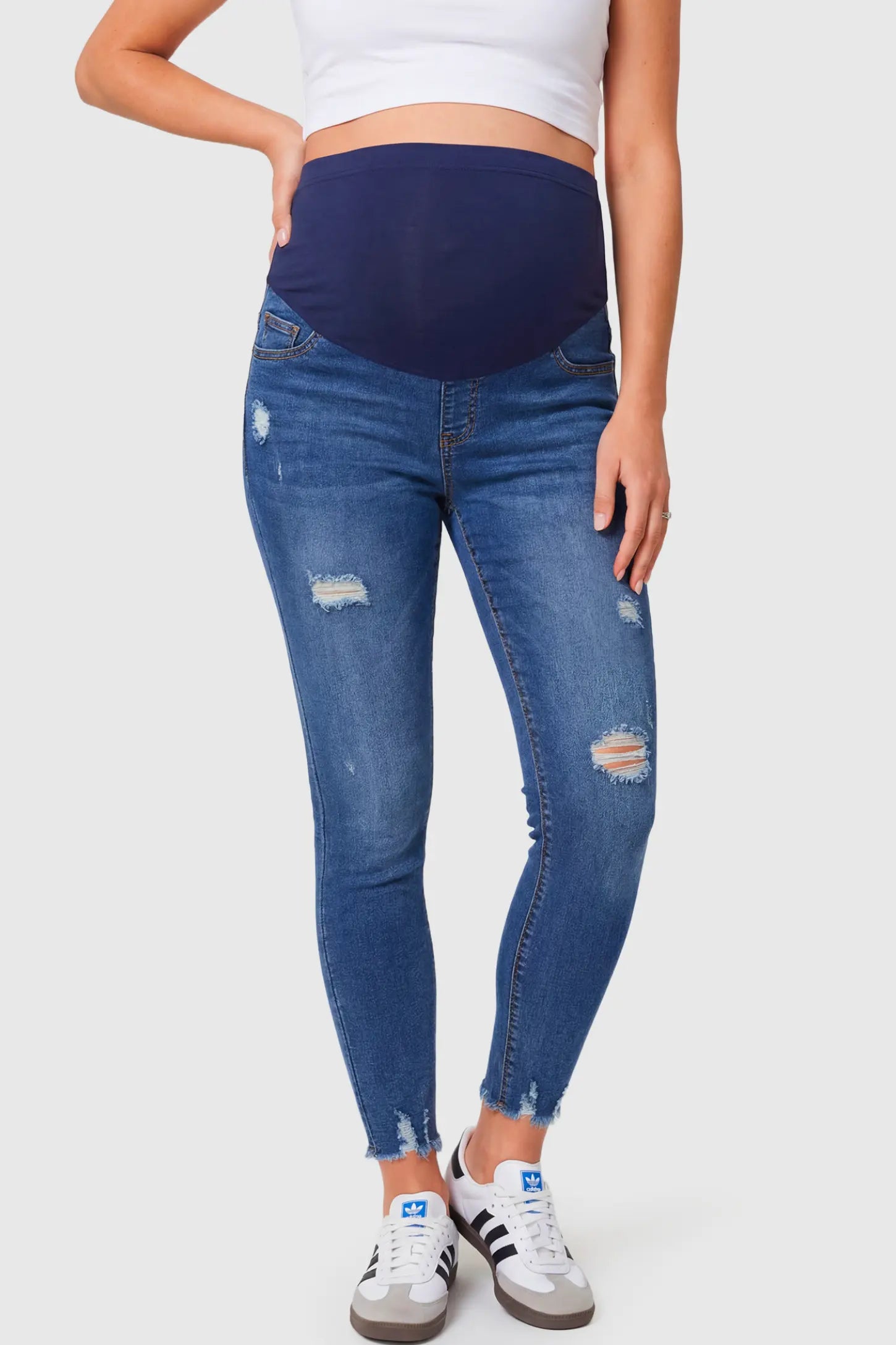 High-Rise Distressed Skinny Maternity Jeans in navy blue featuring over-the-belly support panel and frayed hem on a pregnant model.