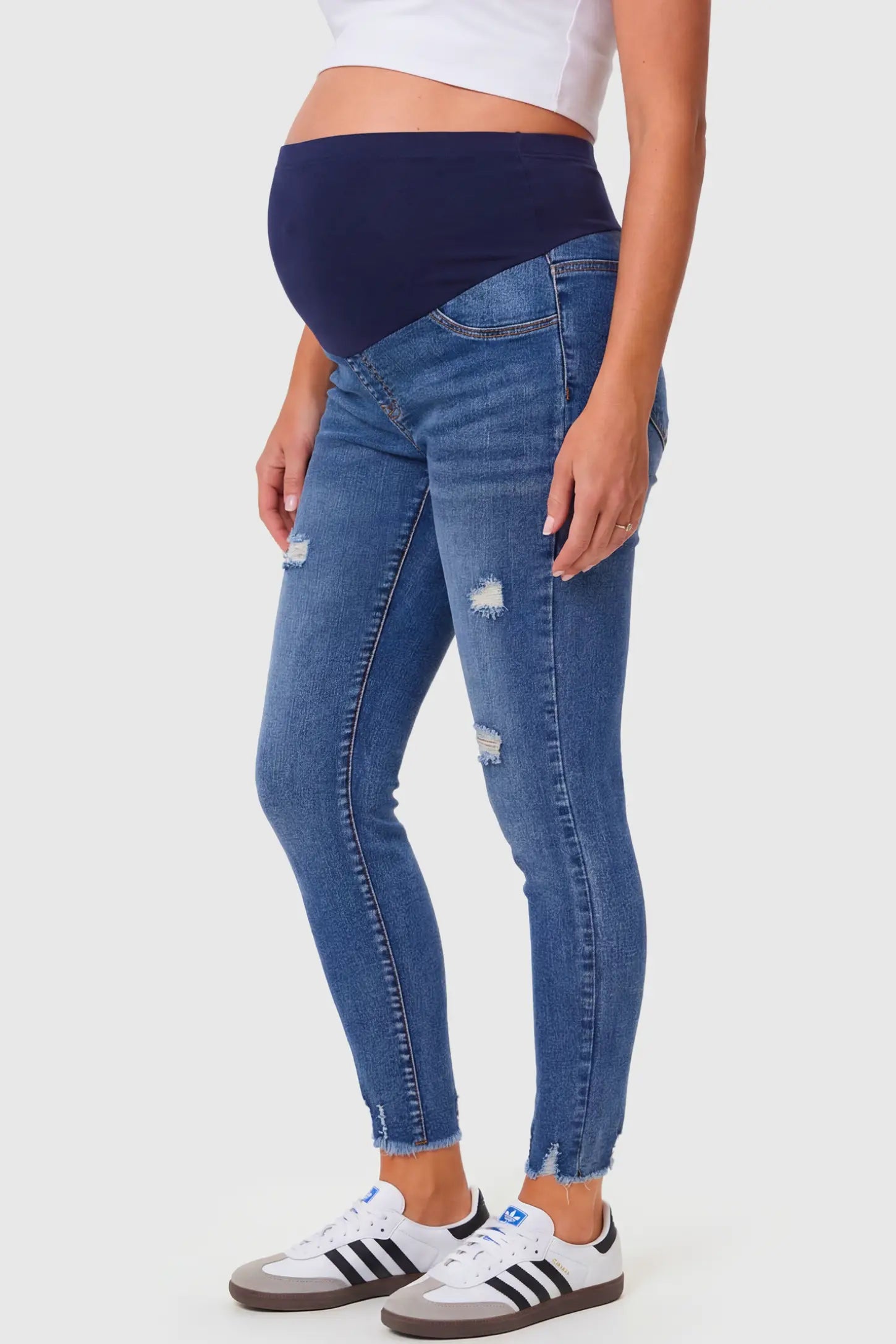 High-Rise Distressed Skinny Maternity Jeans High-Rise Distressed Skinny Maternity Jeans in navy blue featuring over-the-belly support panel and frayed hem on a pregnant model.