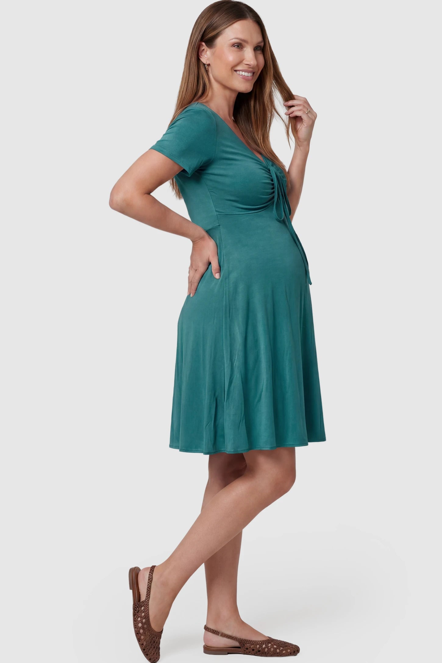 Drawstring Bow Front A‑Line Maternity Short Dress Drawstring bow front A-line maternity short dress in teal green with bump-friendly relaxed fit, side view on pregnant model