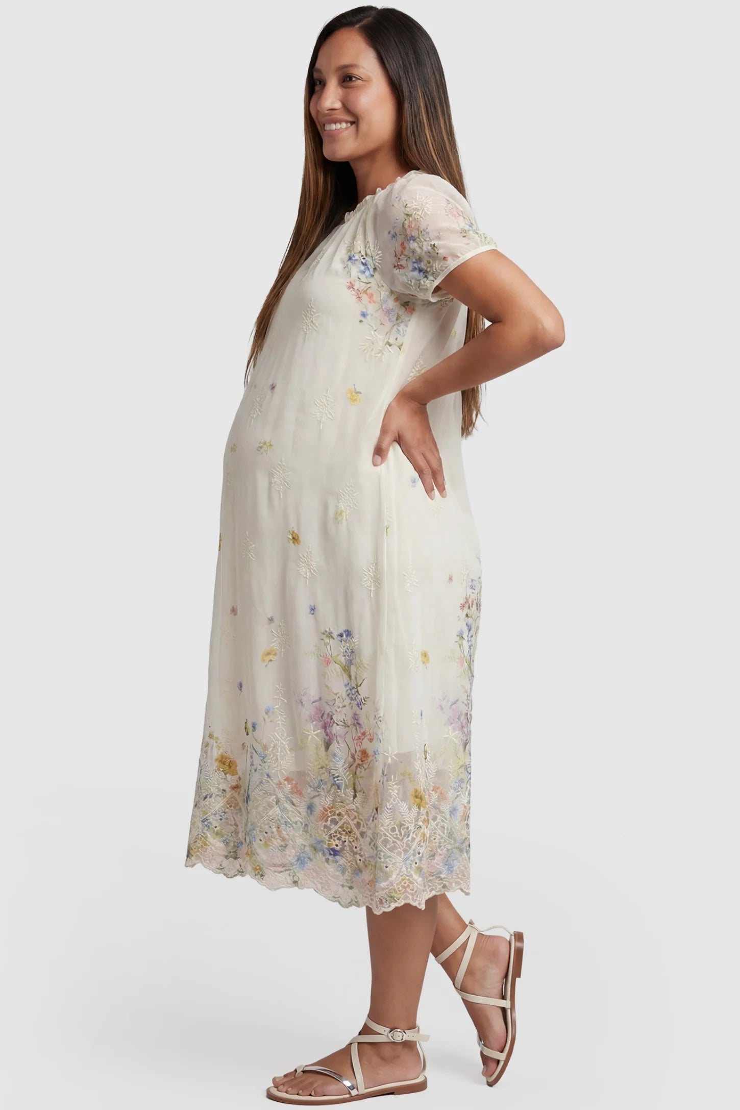 Embroidered Floral Convertible Neckline Maternity Midi Dress Embroidered floral convertible neckline maternity midi dress in beige with embroidered floral detail and puff sleeves, side view on pregnant model