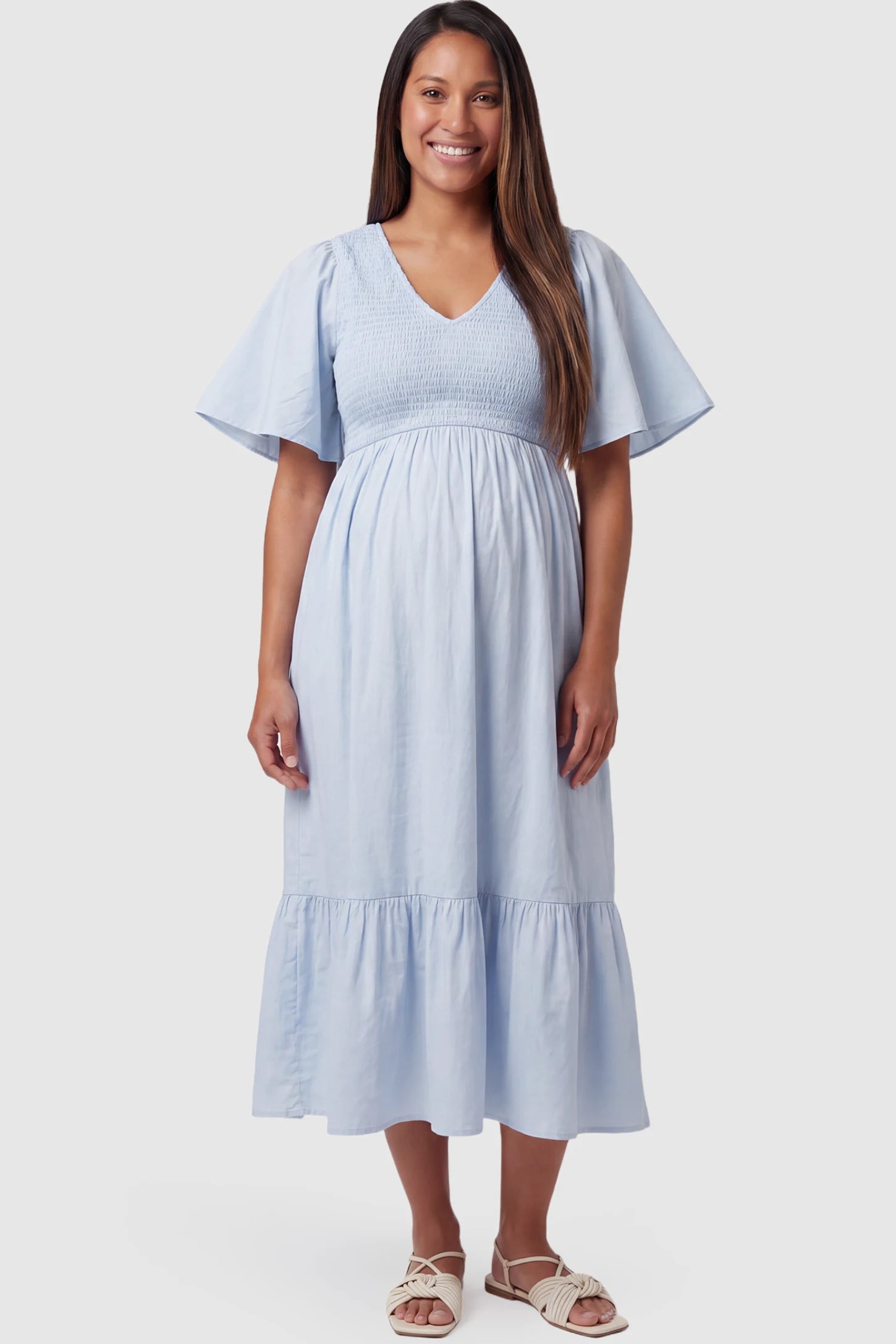 Smocked Empire Waist Tiered Skirt Maternity Midi Dress Smocked empire waist tiered skirt maternity midi dress in light blue with V-neckline and stretchy smocked bodice, front view on pregnant model