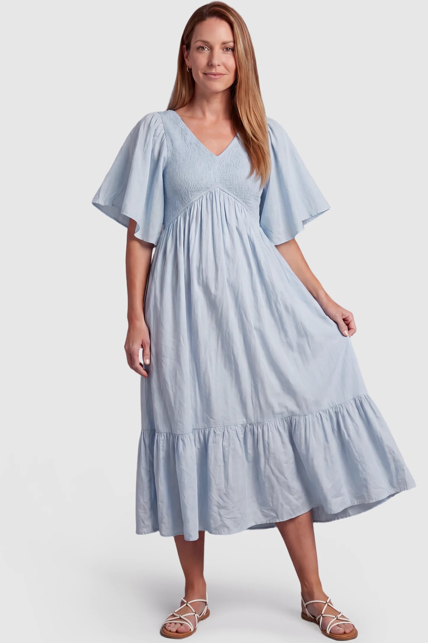 Smocked Empire Waist Tiered Skirt Maternity Midi Dress Smocked empire waist tiered skirt maternity midi dress in light blue with V-neckline and stretchy smocked bodice, front view on postpartum model