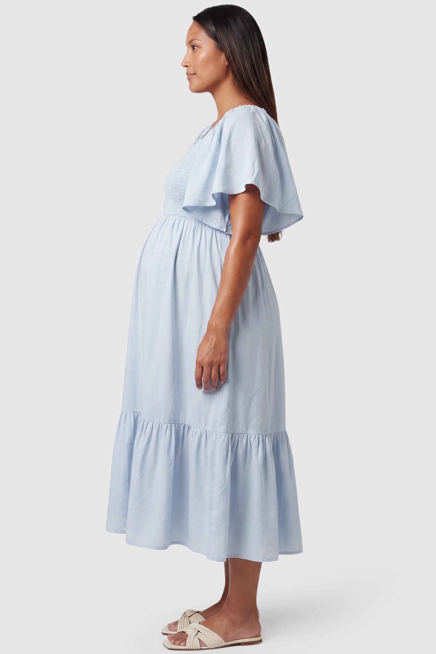 Smocked Empire Waist Tiered Skirt Maternity Midi Dress Smocked empire waist tiered skirt maternity midi dress in light blue with bump-friendly empire waist fit, side view on pregnant model