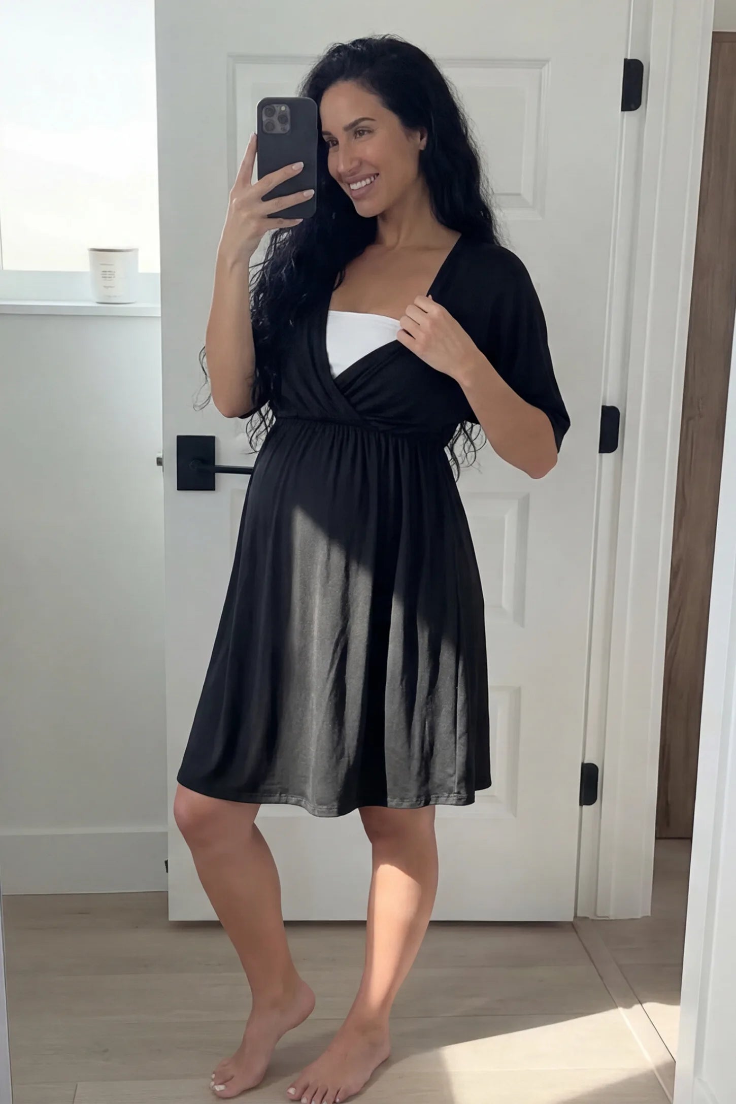 Wrap Front Empire Waist Maternity & Nursing Mini Dress Wrap Front Empire Waist Maternity & Nursing Dress in black featuring a draped crossover V-neck and short sleeves on pregnant model.