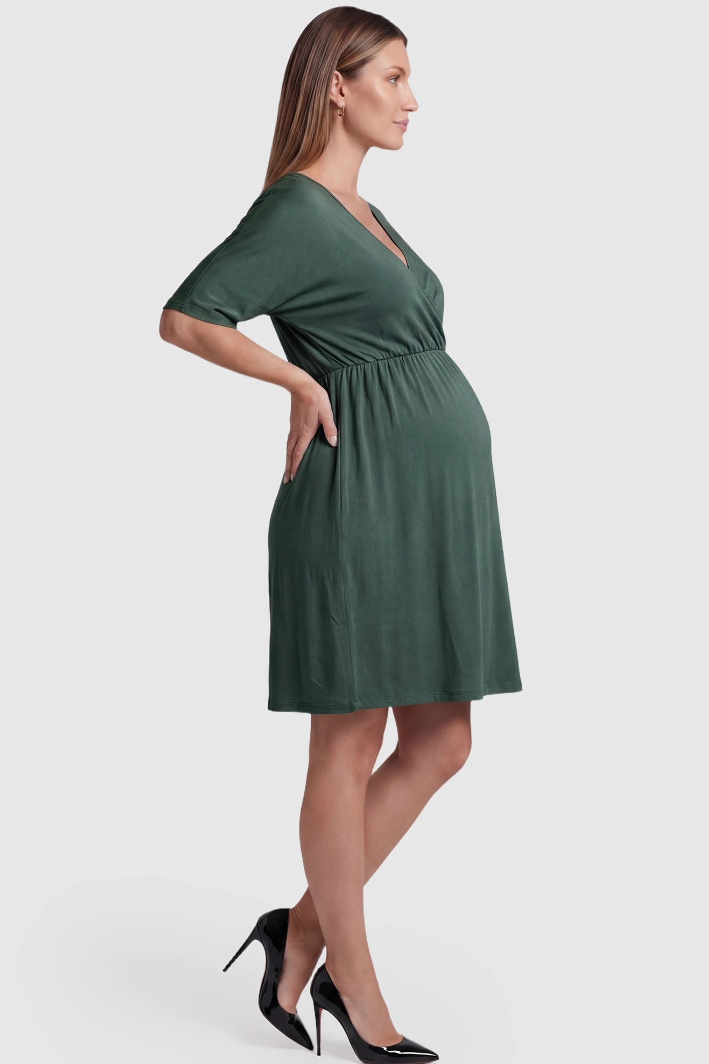 Wrap Front Empire Waist Maternity & Nursing Dress in dark green featuring a draped crossover V-neck and short sleeves on pregnant model side view.