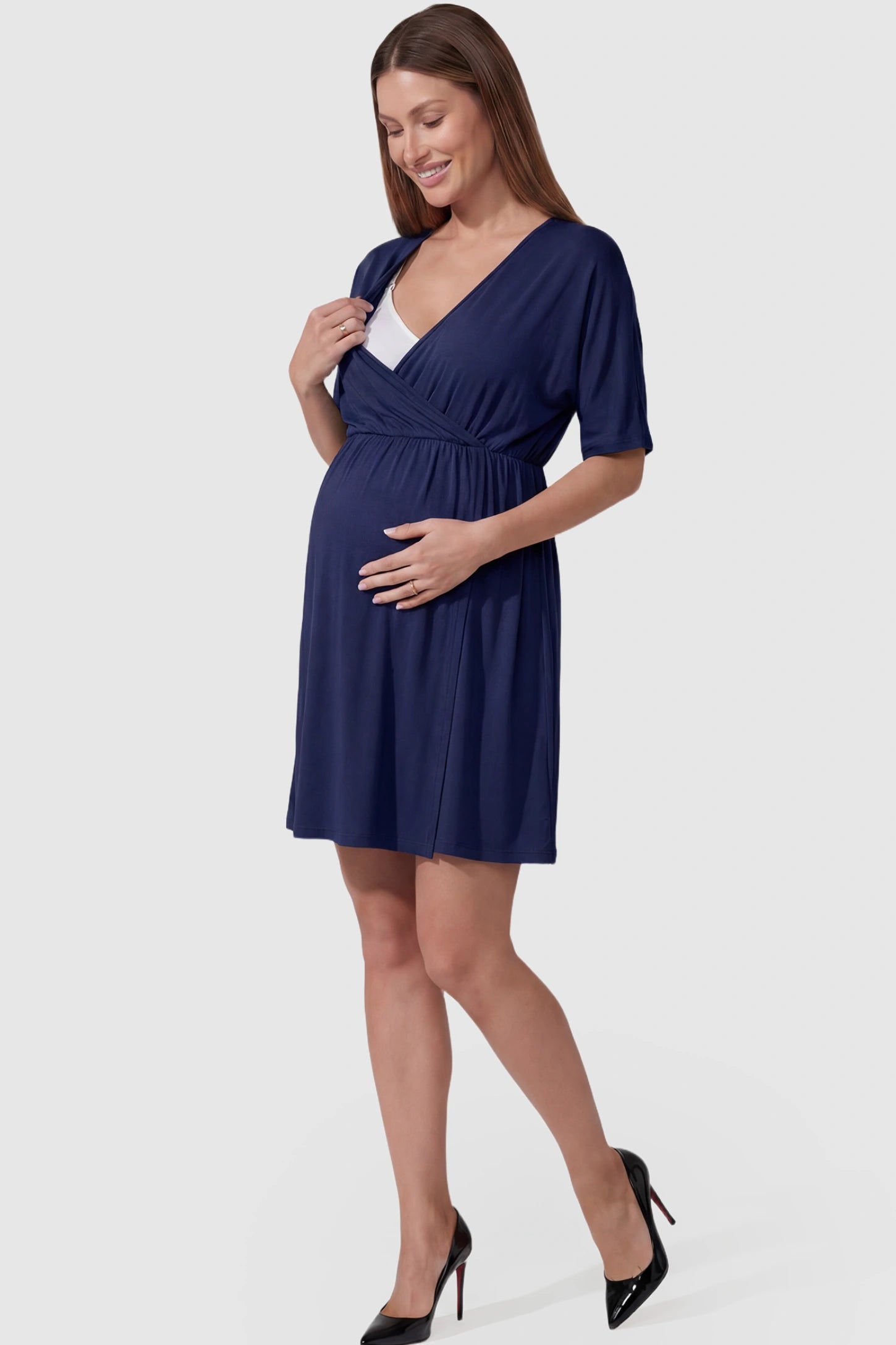 Wrap Front Empire Waist Maternity & Nursing Mini Dress Wrap Front Empire Waist Maternity & Nursing Dress in navy blue featuring a draped crossover V-neck and short sleeves on pregnant model.