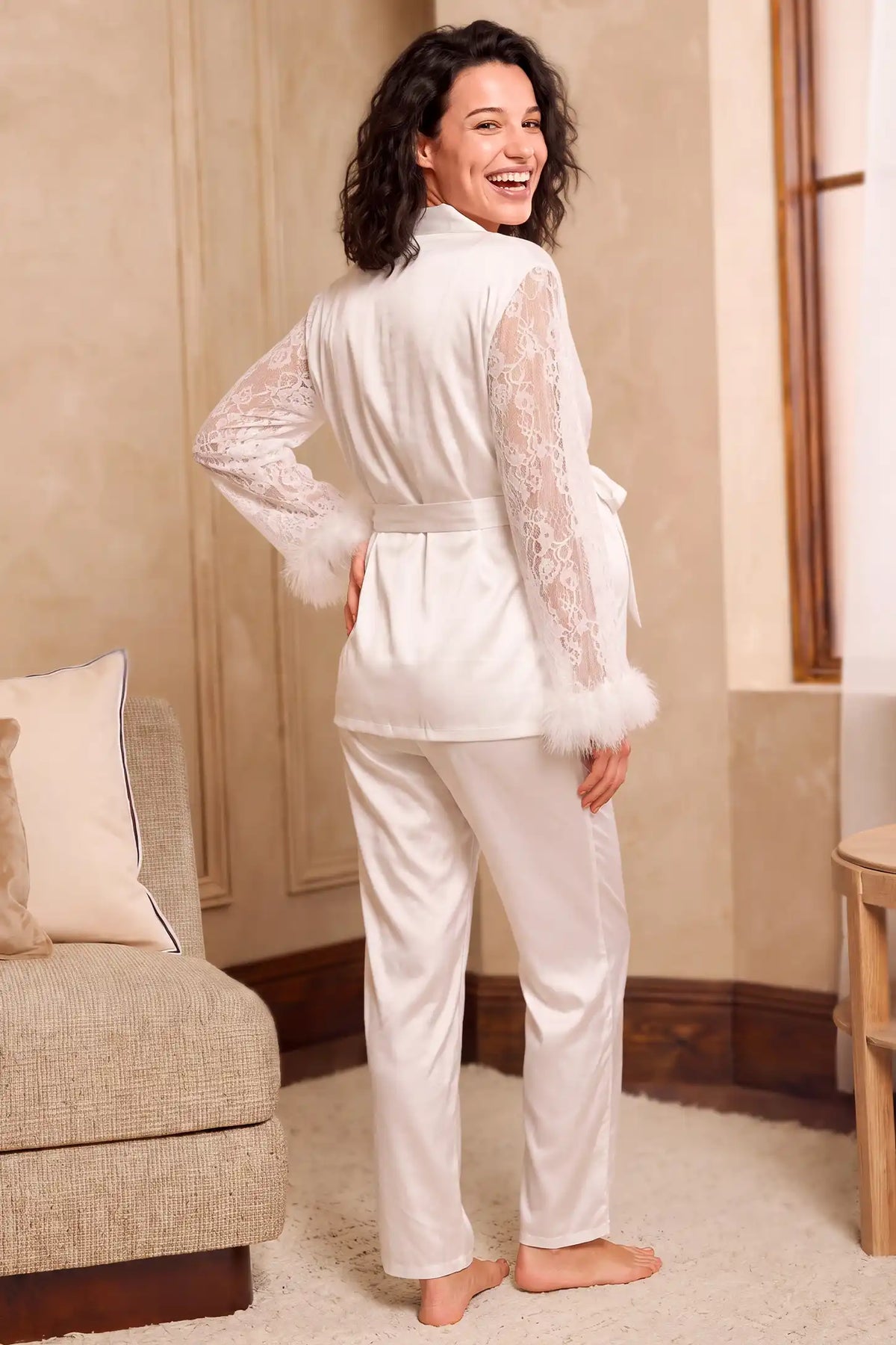 Feather-Trim Satin Maternity Pajama Set in White featuring sheer lace long sleeves, feather-trimmed cuffs, tie-waist wrap top, and straight-leg satin-look pants with full back coverage on a model, back view.