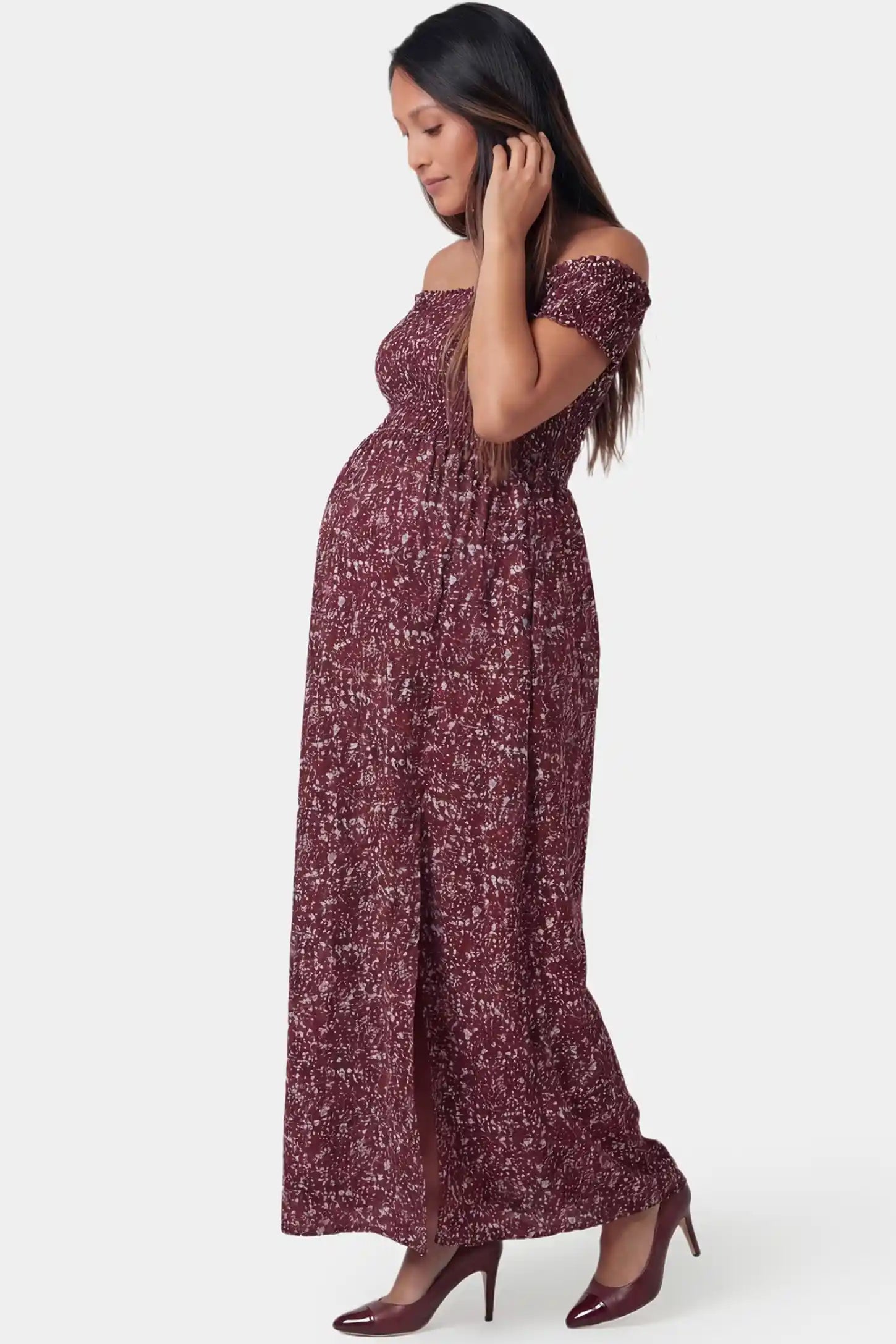 Floral Off-Shoulder Smocked Bodice Maxi Maternity Dress Floral off-shoulder smocked bodice maxi maternity dress in burgundy featuring a flowy silhouette in side view on a pregnant model