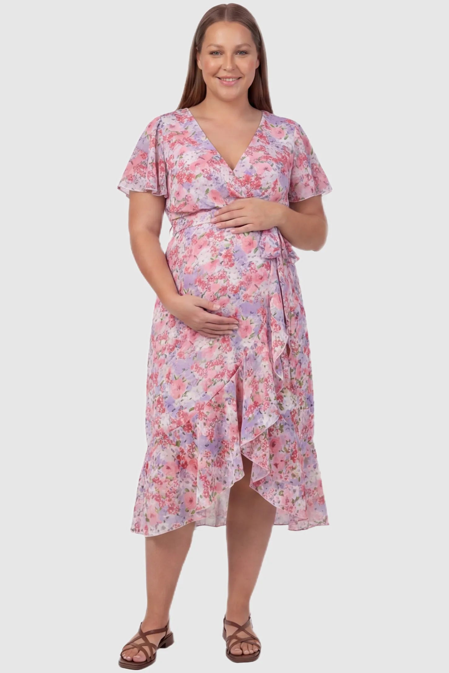 Floral V-Neck Ruffled Hem Midi Maternity Dress Floral V-neck ruffled hem midi maternity dress in pink featuring V-neckline and tie waist in full body front view on a plus size pregnant model, front view.
