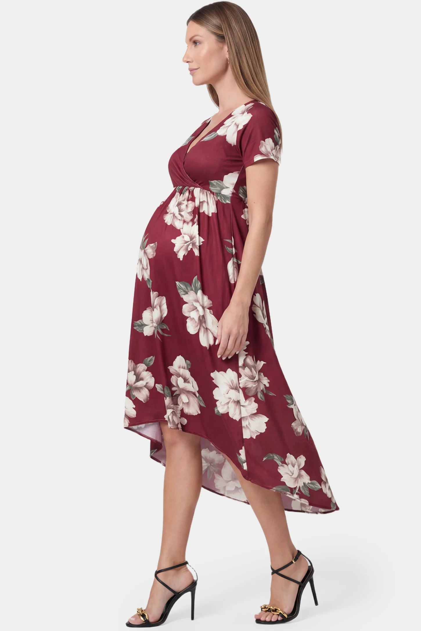 Floral V-neck wrap high-low maxi maternity dress in wine red floral featuring dramatic high-low hemline in side view on a pregnant model