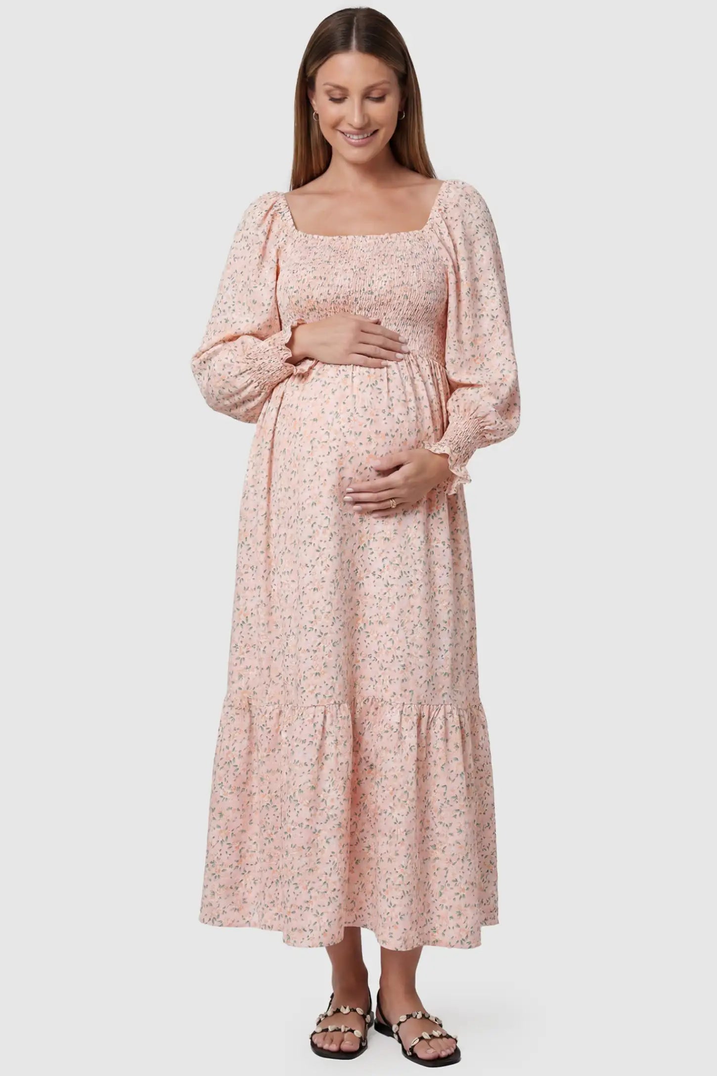 Floral Smocked Tiered Maternity Midi Dress in pink floral print featuring a square neckline, puff sleeves, and a tiered midi skirt on a pregnant model, front view.