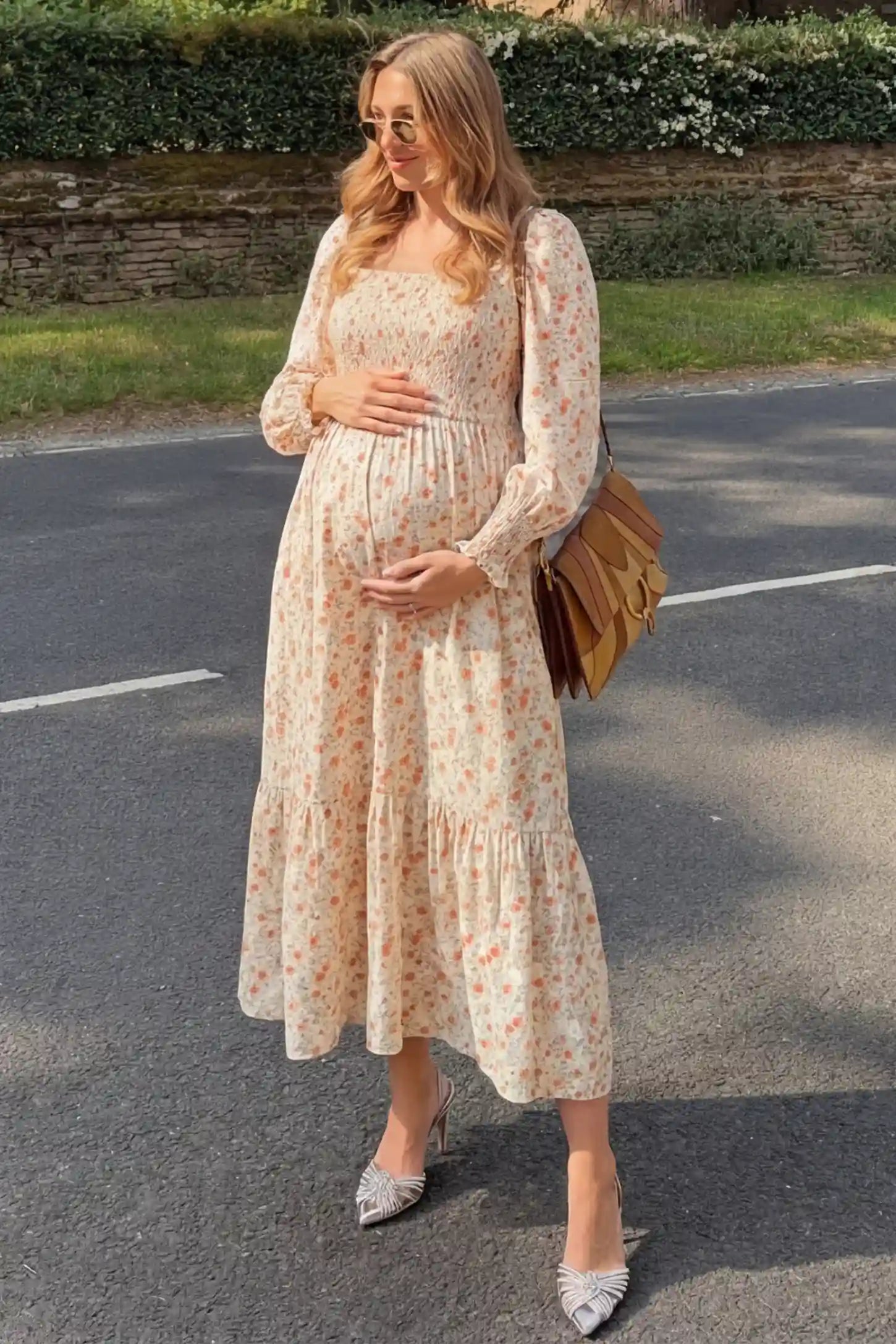 Floral Smocked Tiered Maternity Midi Dress in white floral print featuring square neckline, puff sleeves, and tiered midi skirt on pregnant woman in outdoor setting, front view