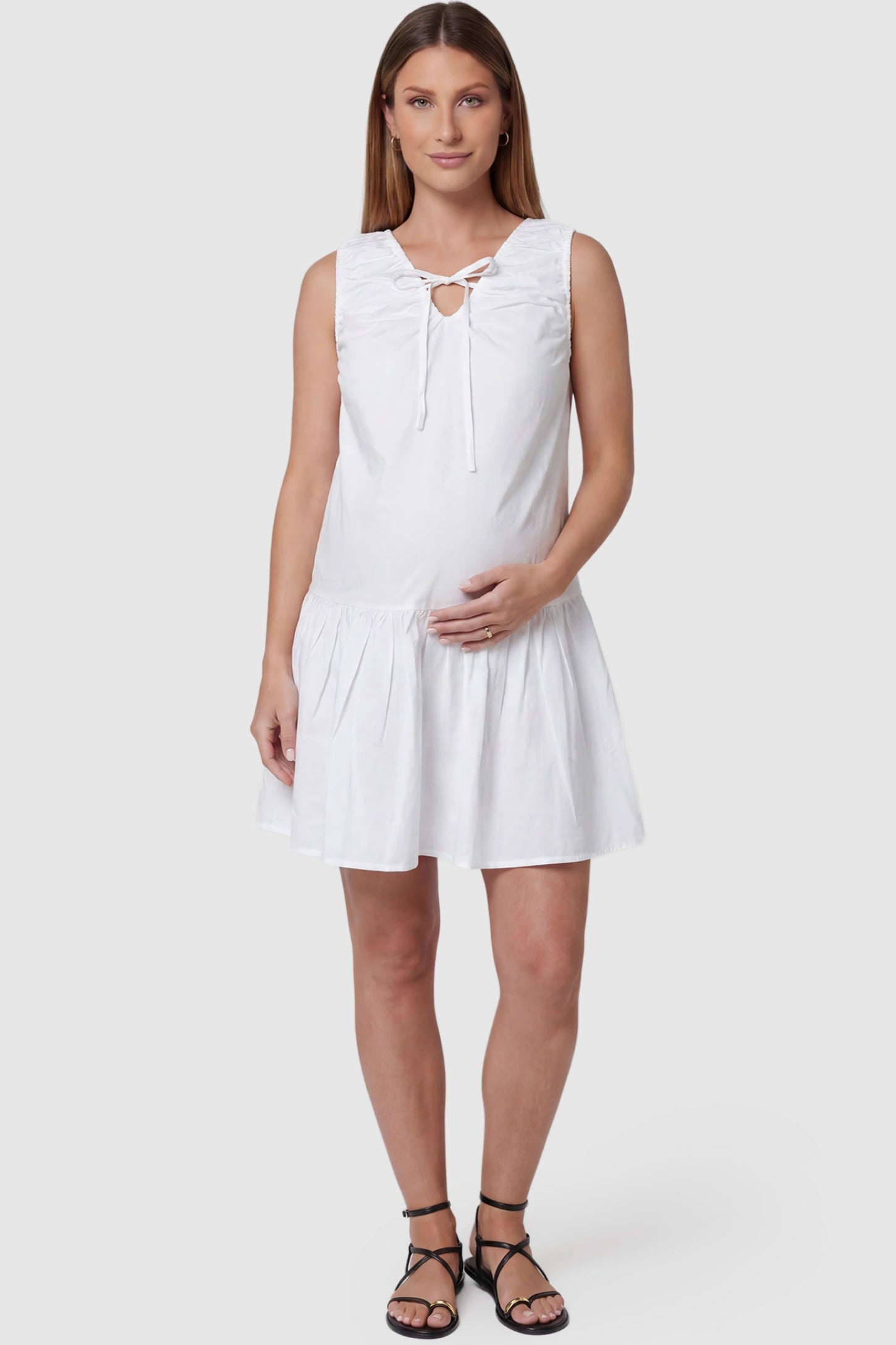 Keyhole tie sleeveless maternity short dress in white with V-neckline and keyhole tie front detail, front view on pregnant model