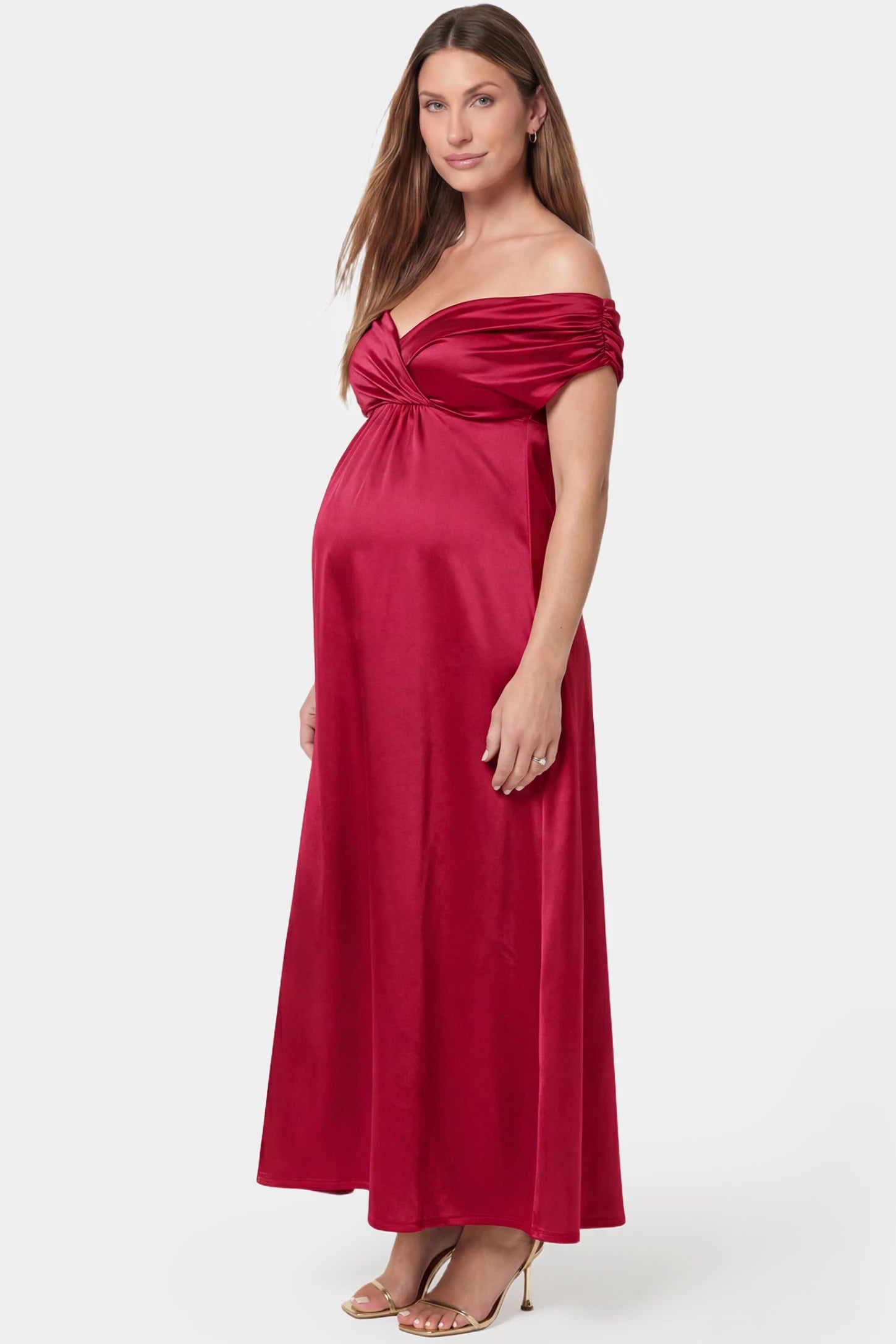 Off-shoulder fitted waist flowing maxi maternity dress in red featuring flowing skirt in side view on a pregnant model