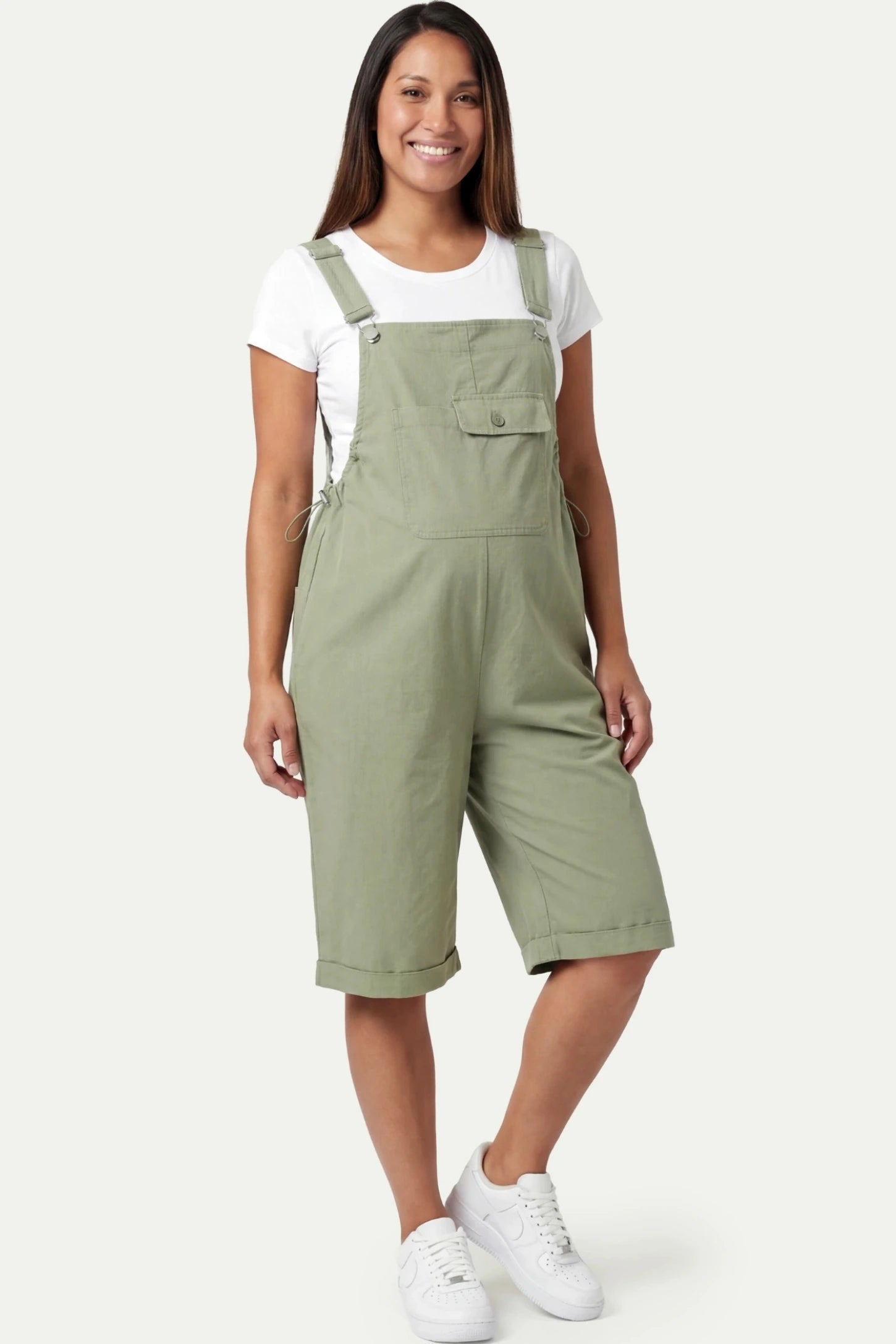 Oversized Front Pocket Maternity Overalls Shorts in Green featuring a front bib pocket on a pregnant model.