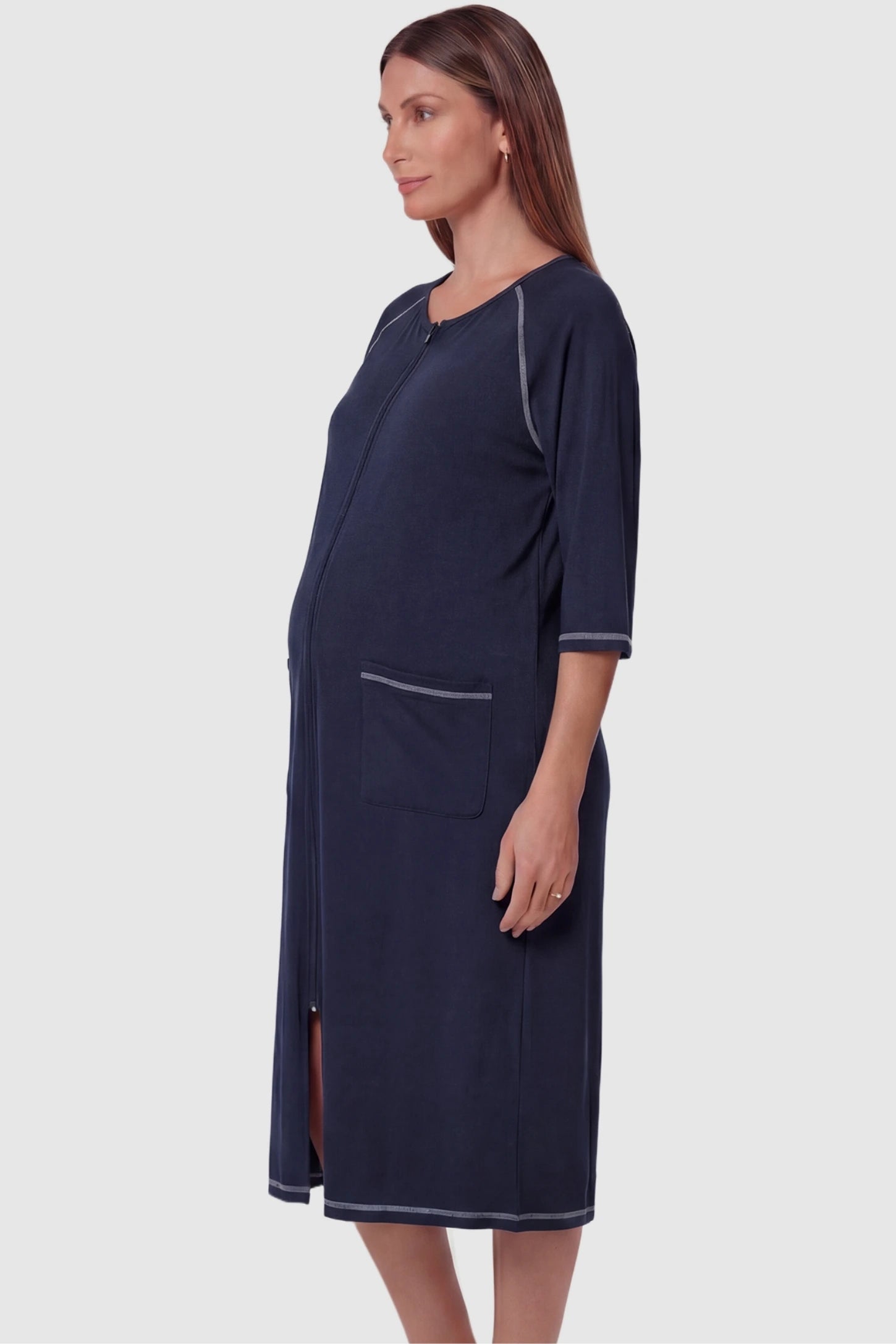 Front zipper three-quarter sleeve midi maternity and nursing dress in navy blue featuring functional pockets and three-quarter sleeves in side view on a pregnant model