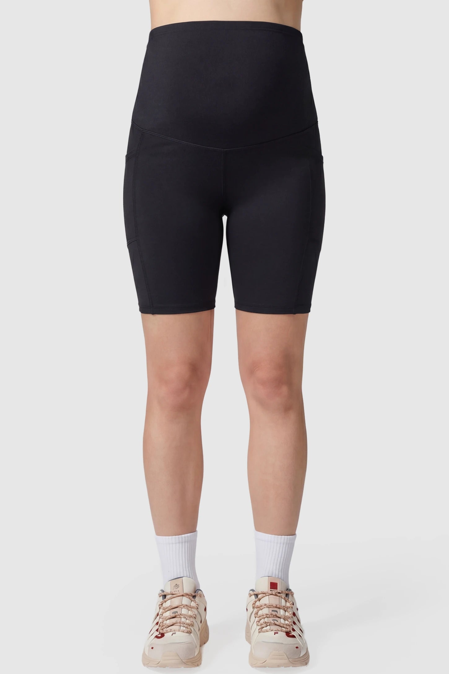 High-rise stretch biker maternity shorts in black featuring seamless fit, mid-thigh length, and supportive belly panel on pregnant model. front view