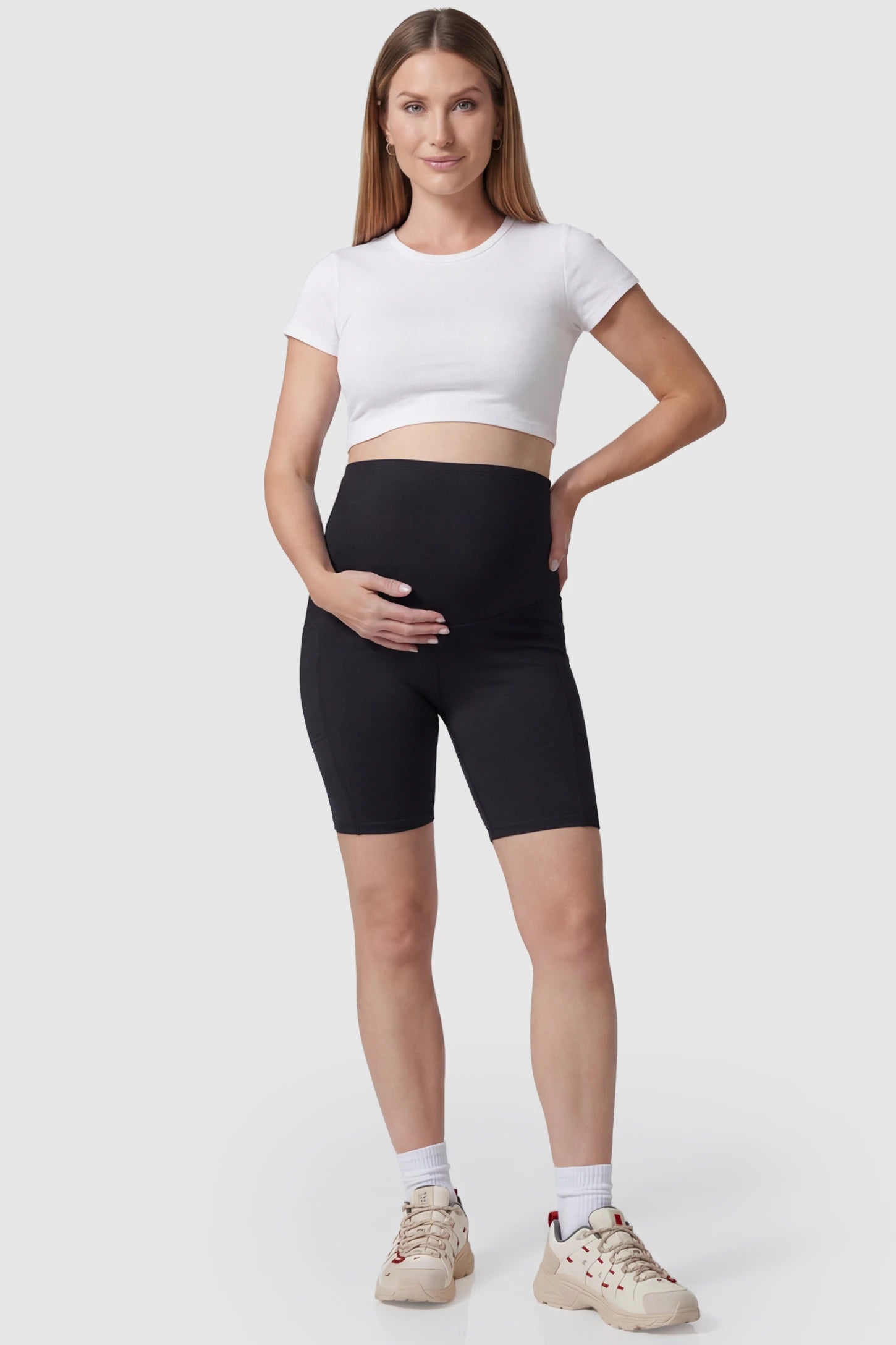 High-rise stretch biker maternity shorts in black featuring seamless fit, mid-thigh length, and supportive belly panel on pregnant model. front view