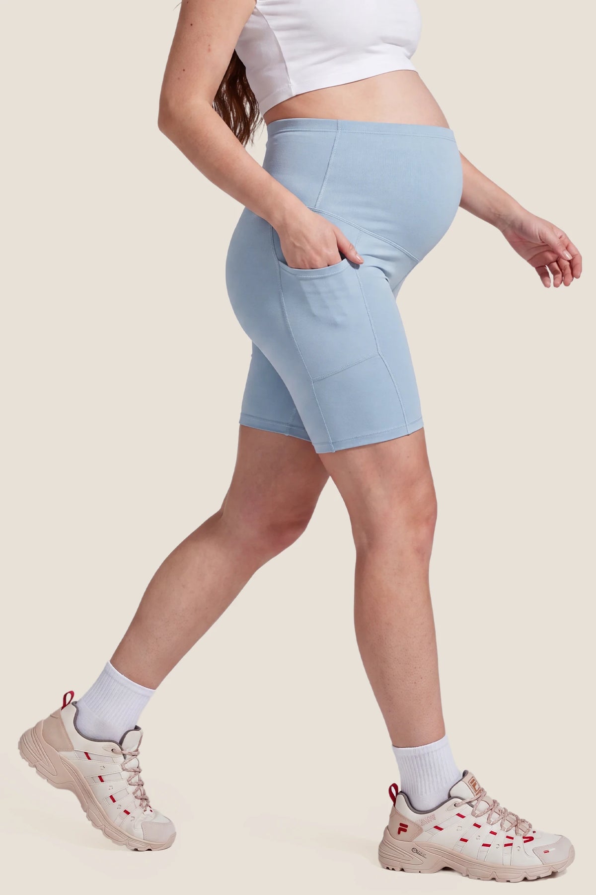 High-Rise Stretch Biker Maternity Shorts High-Rise Stretch Biker Maternity Shorts in Sky Blue featuring functional side pocket, seam-contoured side fit, and supportive maternity stretch coverage on a pregnant model, side view.