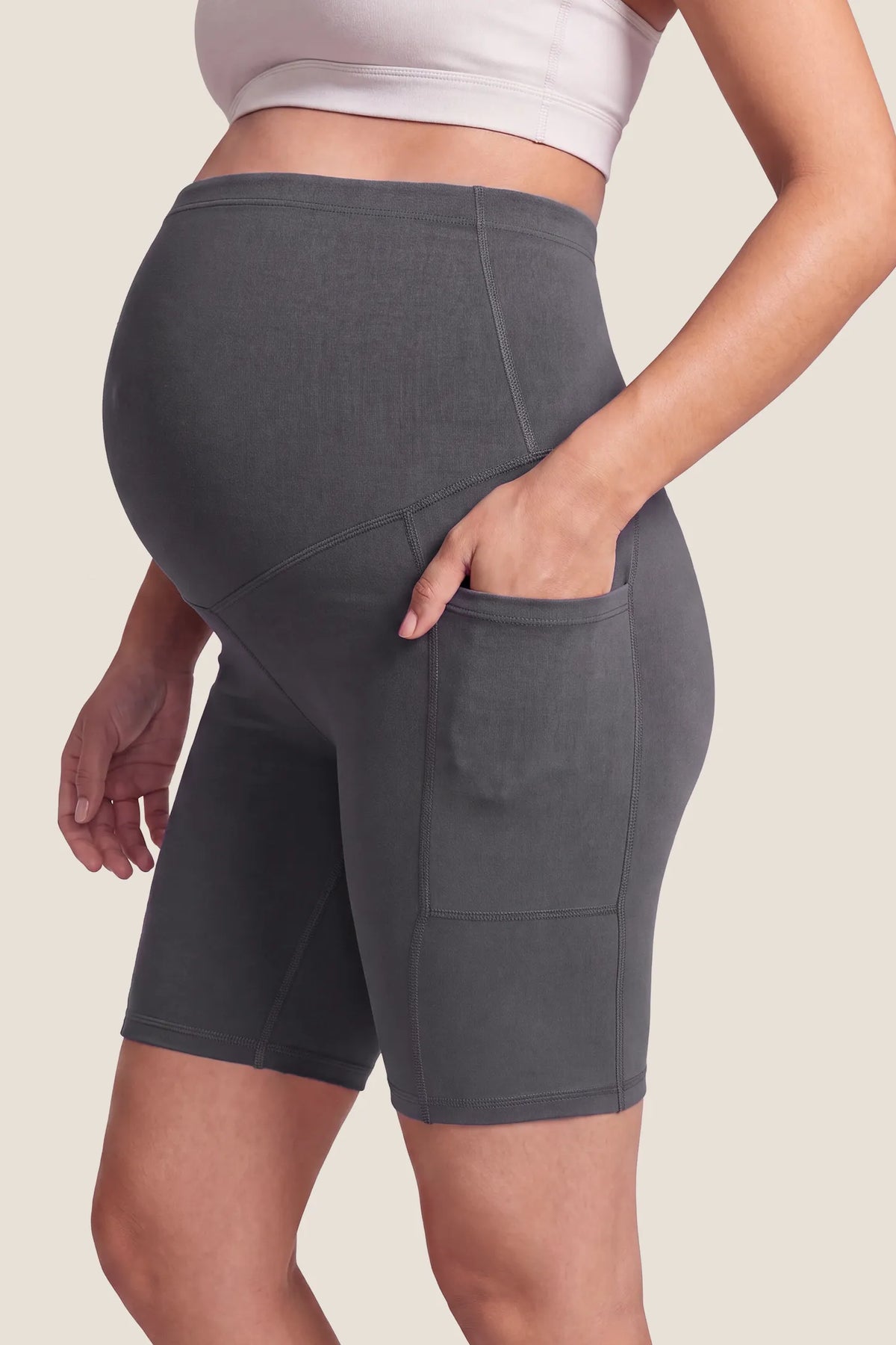 High-Rise Stretch Biker Maternity Shorts High-Rise-Stretch-Biker-Maternity-Shorts in Dark Gray featuring seam-contoured side details, functional side pocket, full belly support coverage, and flexible maternity stretch fit on a pregnant model, side view.