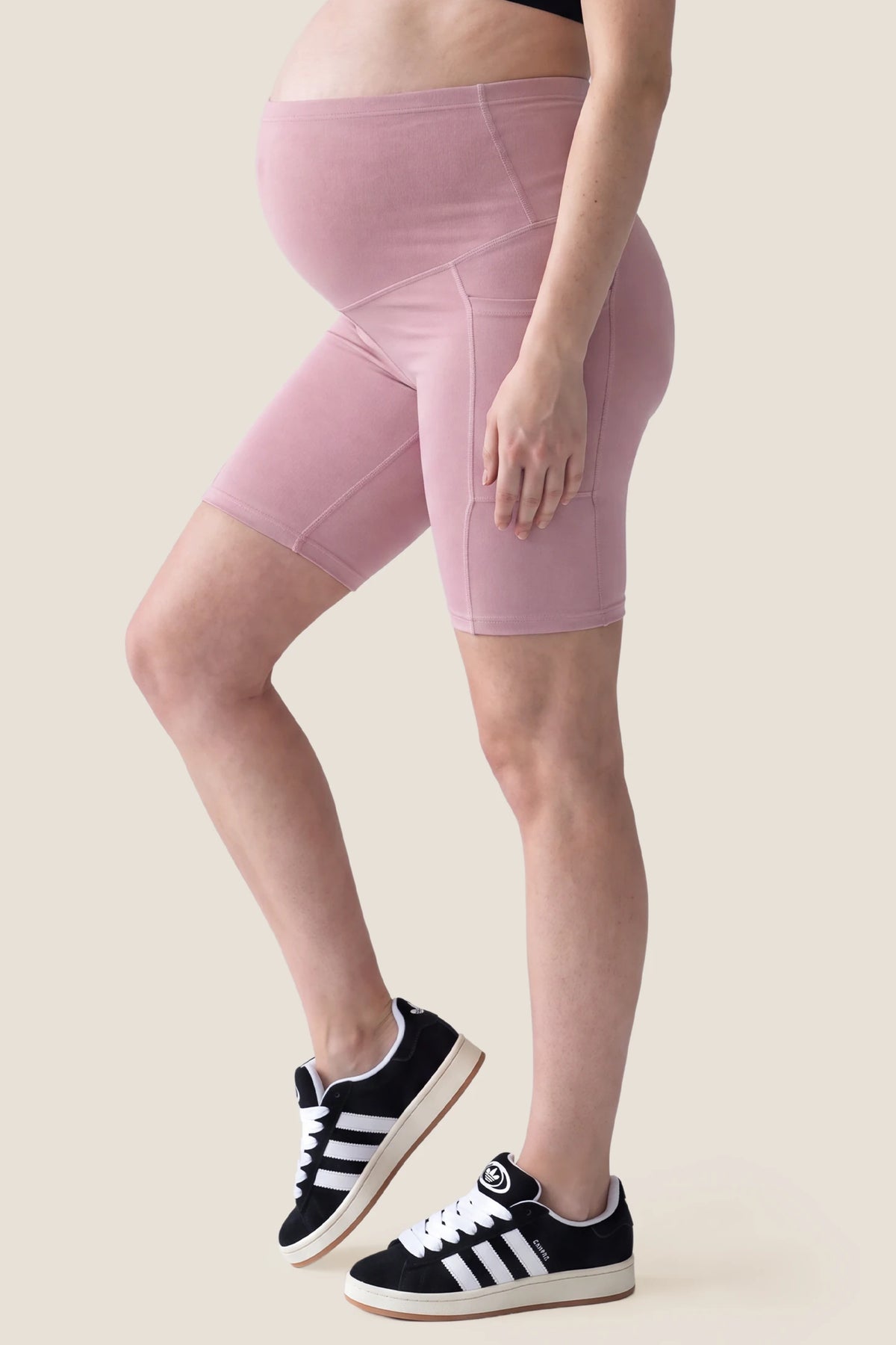 High-Rise Stretch Biker Maternity Shorts High-Rise Stretch Biker Maternity Shorts in Pink featuring functional side pocket, seam-contoured side fit, and supportive maternity stretch coverage on a pregnant model, side view.