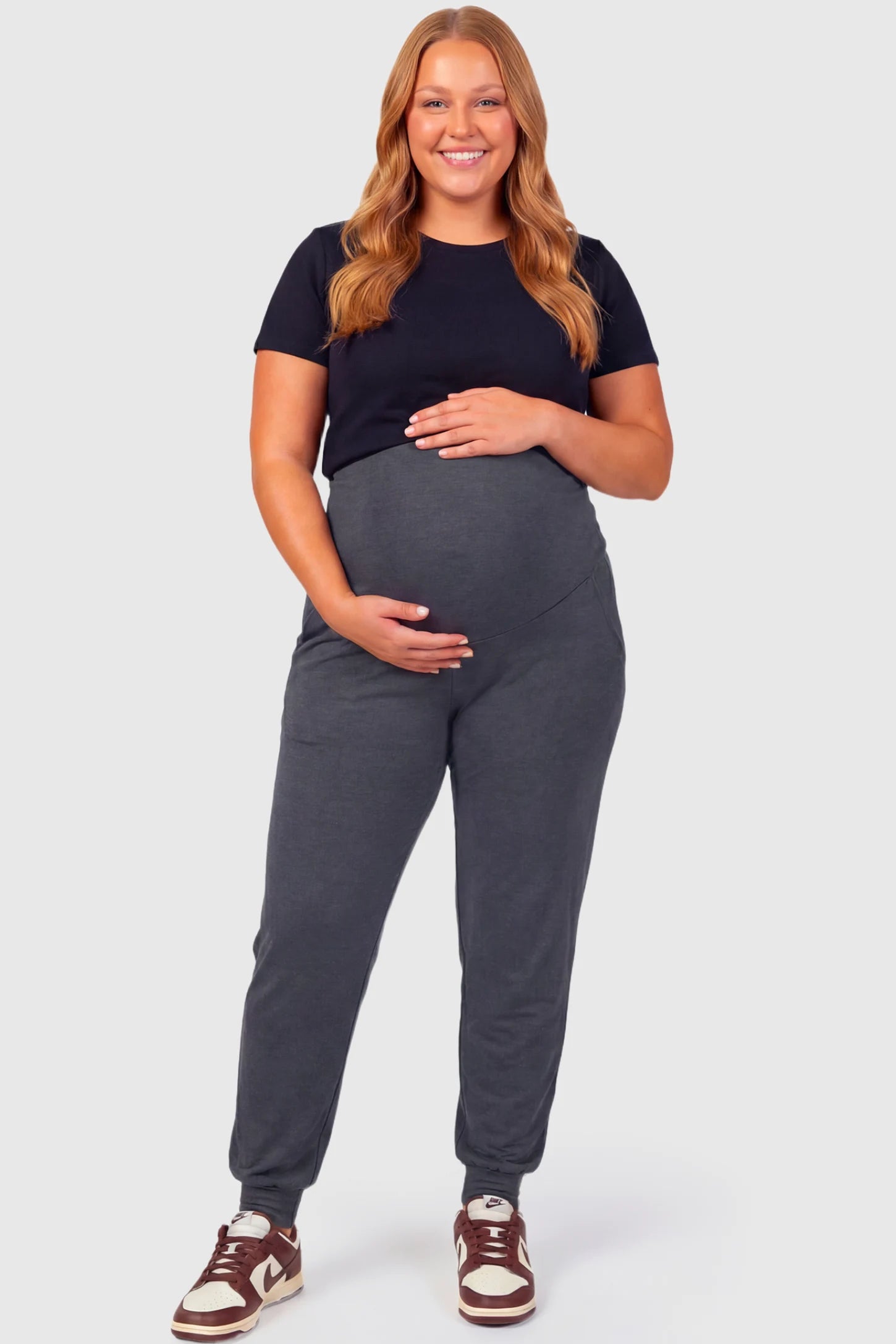 Full-Panel Cuffed Maternity Joggers Full-Panel Cuffed Maternity Joggers in dark gray featuring high-rise over-the-belly panel, ribbed cuff hem, and side pockets on plus size pregnant model.