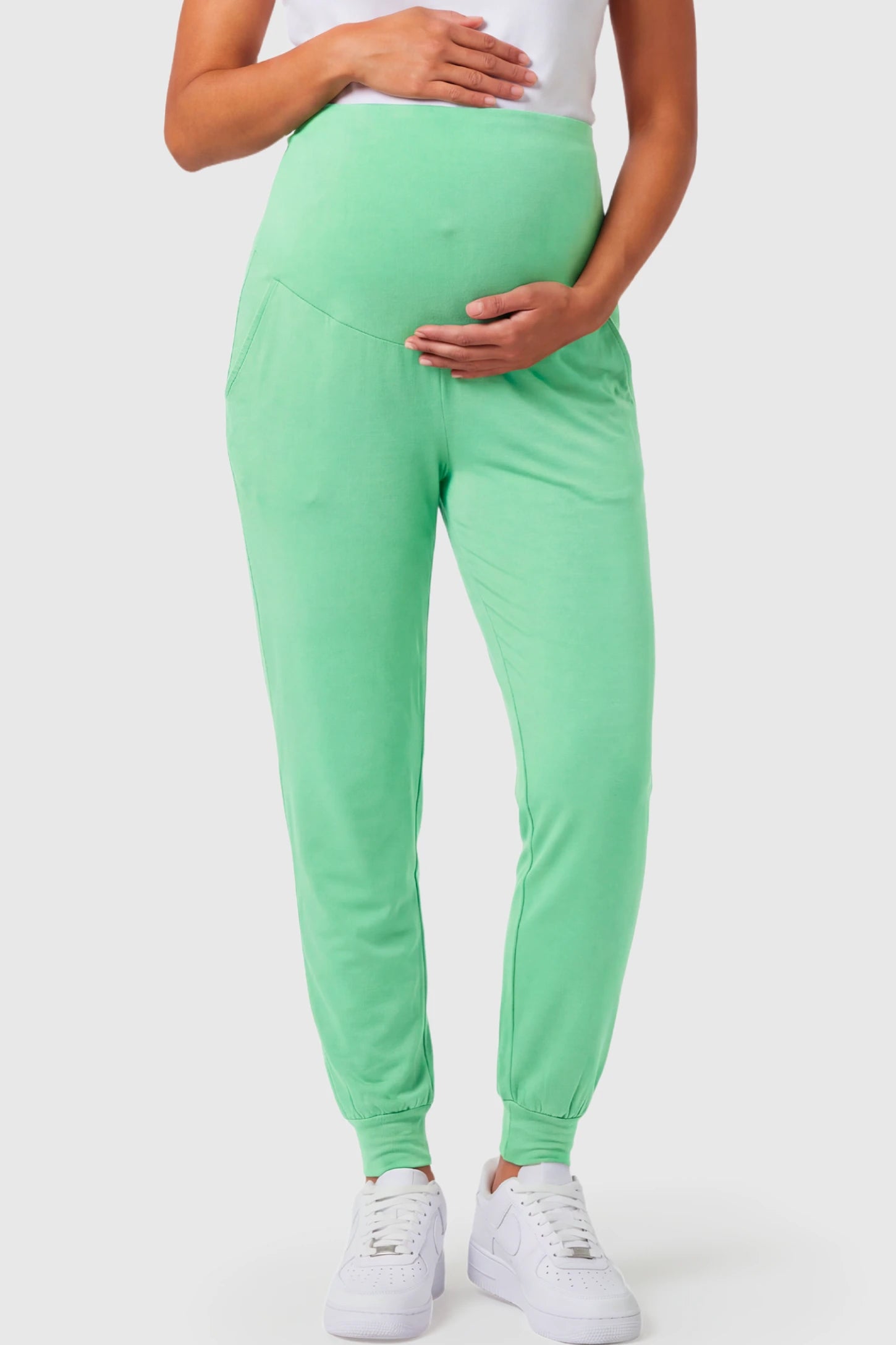 Full-Panel Cuffed Maternity Joggers Full-Panel Cuffed Maternity Joggers in light green featuring high-rise over-the-belly panel, ribbed cuff hem, and side pockets on pregnant model.