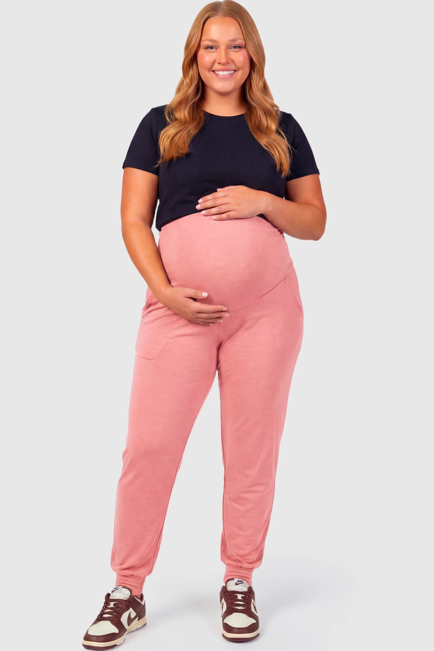 Full-Panel Cuffed Maternity Joggers Full-Panel Cuffed Maternity Joggers in pink featuring high-rise over-the-belly panel, ribbed cuff hem, and side pockets on plus size pregnant model.
