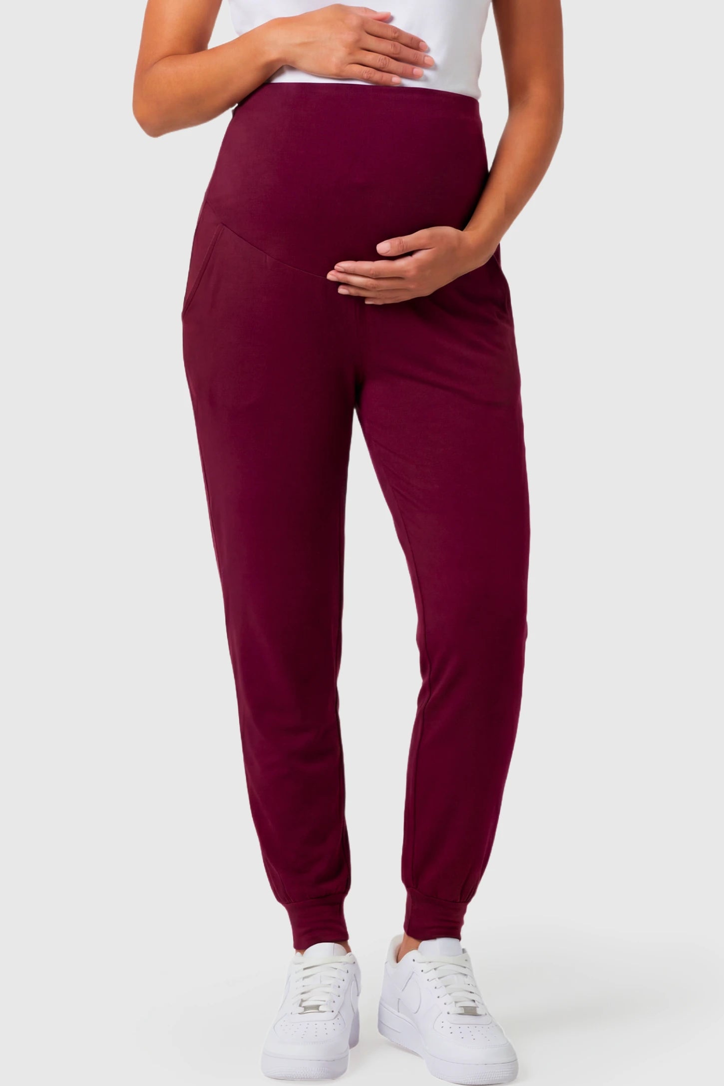 Full-Panel Cuffed Maternity Joggers in wine red featuring high-rise over-the-belly panel, ribbed cuff hem, and side pockets on pregnant model.