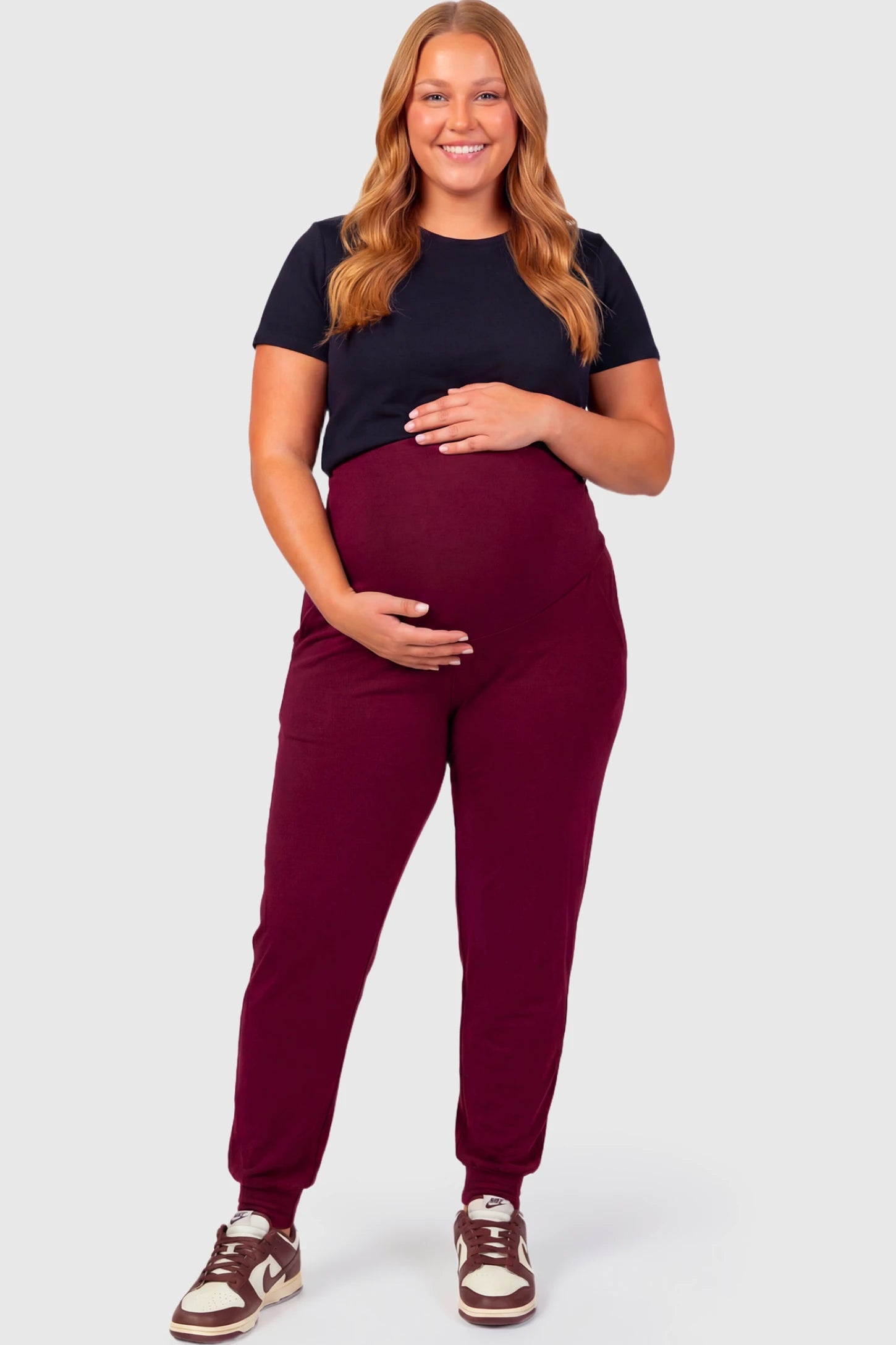 Full-Panel Cuffed Maternity Joggers Full-Panel Cuffed Maternity Joggers in wine red featuring high-rise over-the-belly panel, ribbed cuff hem, and side pockets on plus size pregnant model.