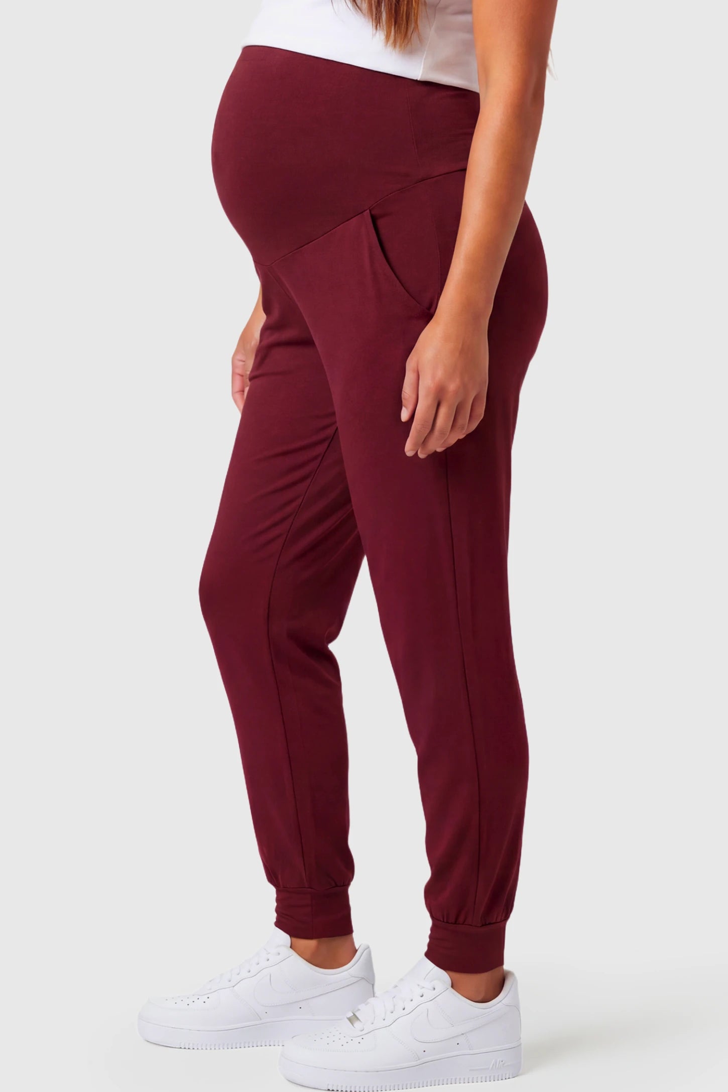 Full-Panel Cuffed Maternity Joggers Full-Panel Cuffed Maternity Joggers in wine red featuring high-rise over-the-belly panel, ribbed cuff hem, and side pockets on pregnant model.