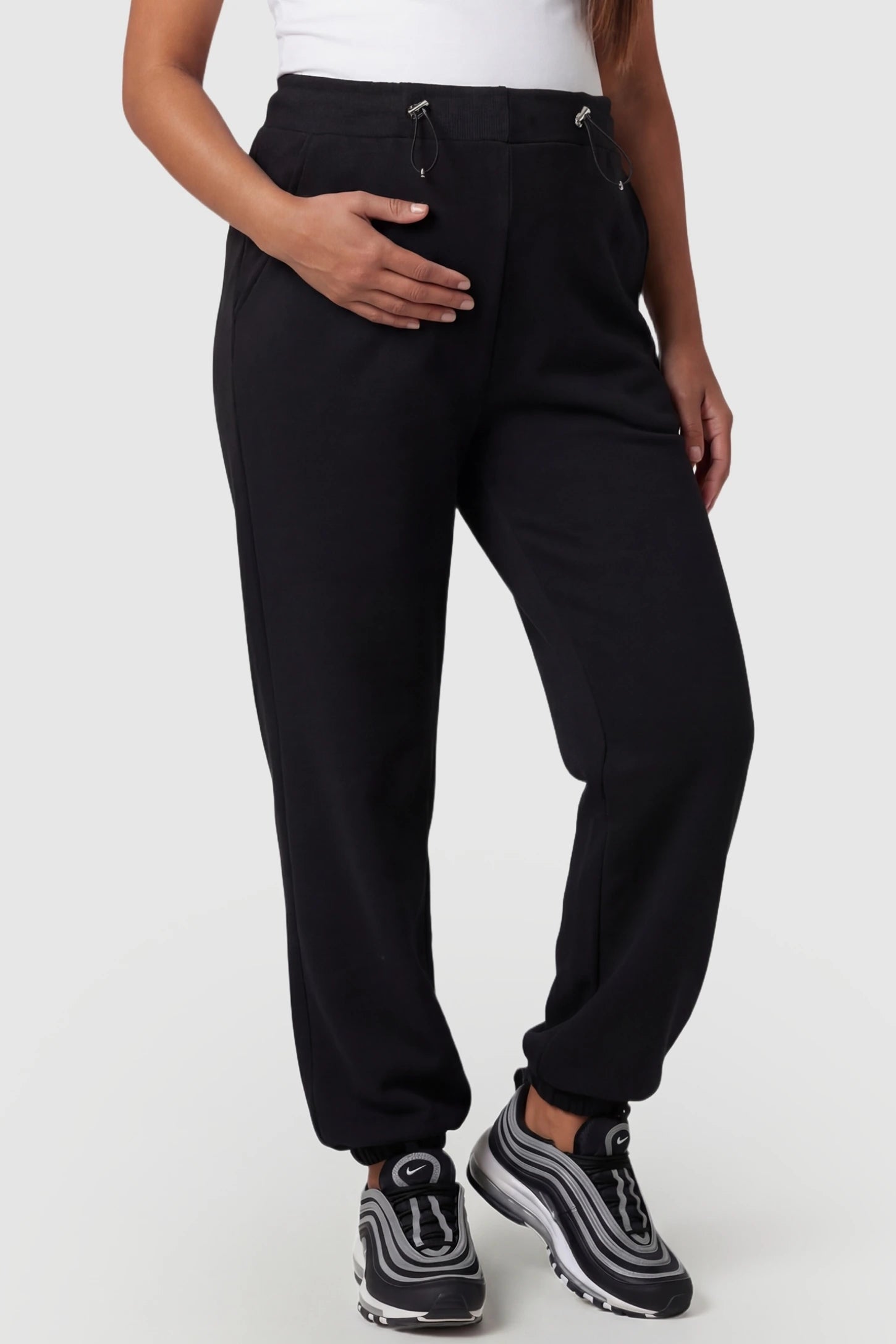 High-rise drawstring waist loose fit jogger maternity pants in black with adjustable drawstring, front view on pregnant model