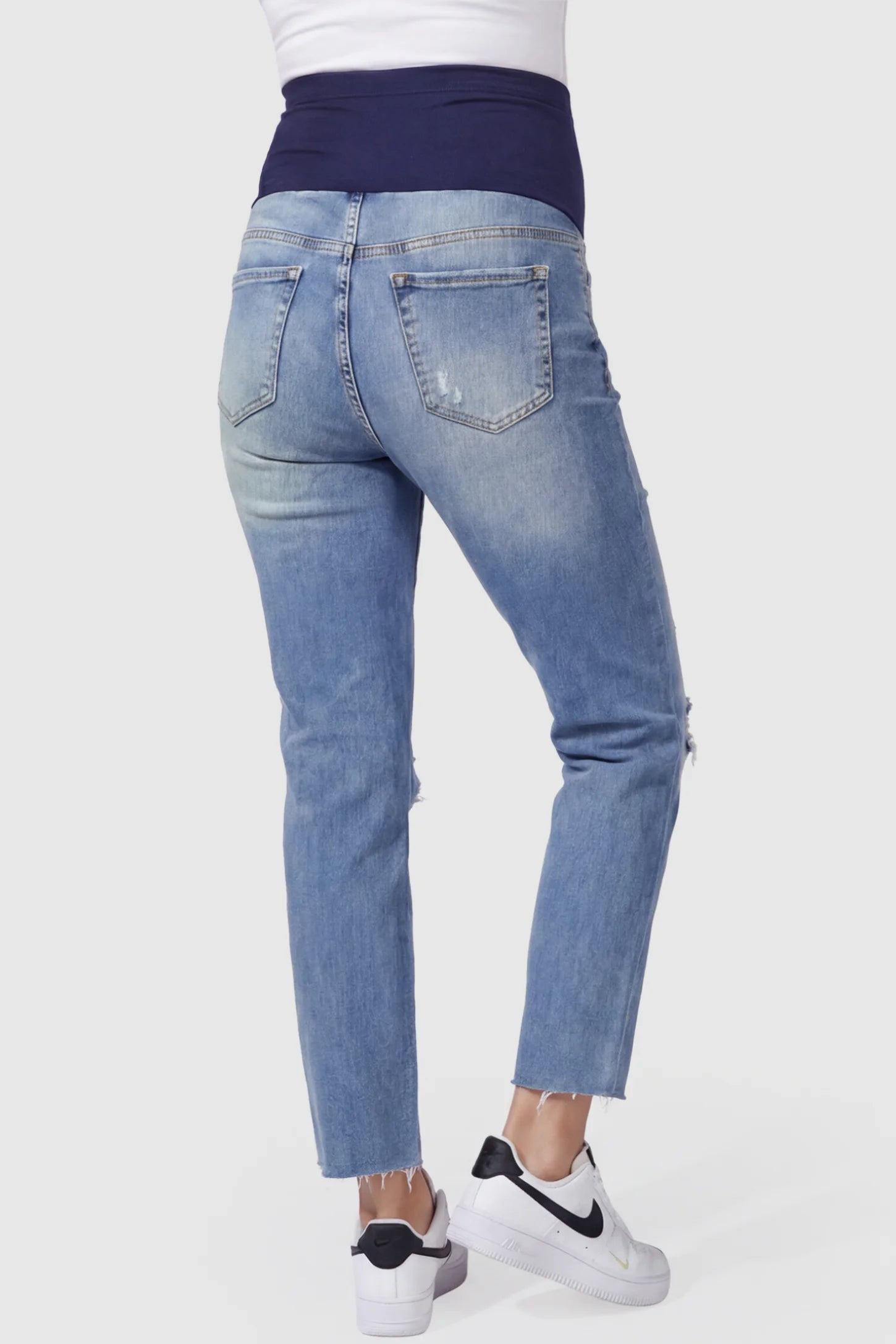 Raw Hem Ankle Straight Leg Maternity Jeans Raw Hem Ankle Straight Leg Maternity Jeans in blue denim featuring high-rise over-the-belly panel and knee-open distressing on pregnant model showing back.