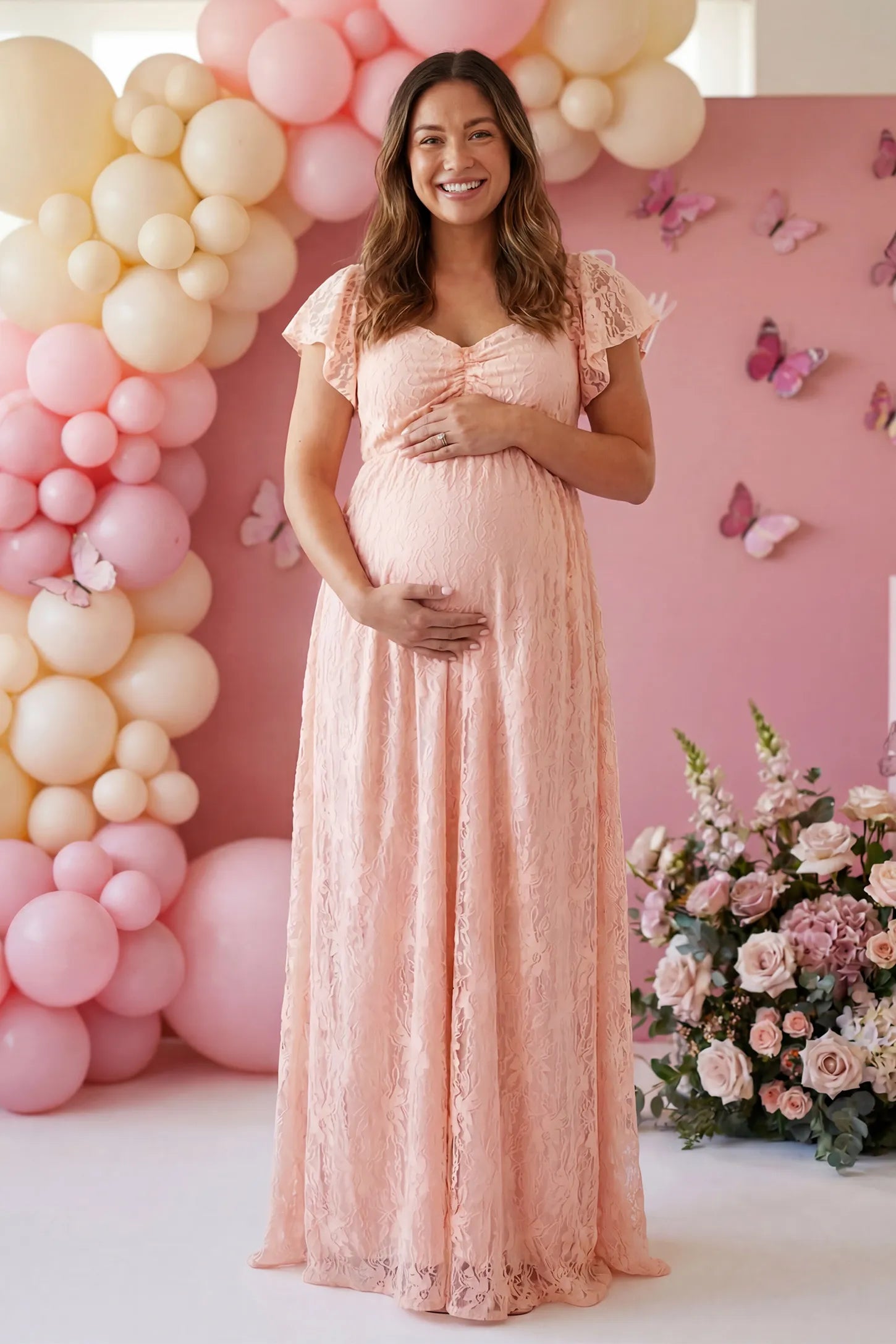 Lace Off Shoulder Maternity Maxi Dress in blush pink featuring a sweetheart neckline with a ruched bust and a full-length skirt, shown on a pregnant woman outdoors on a lawn, side view.