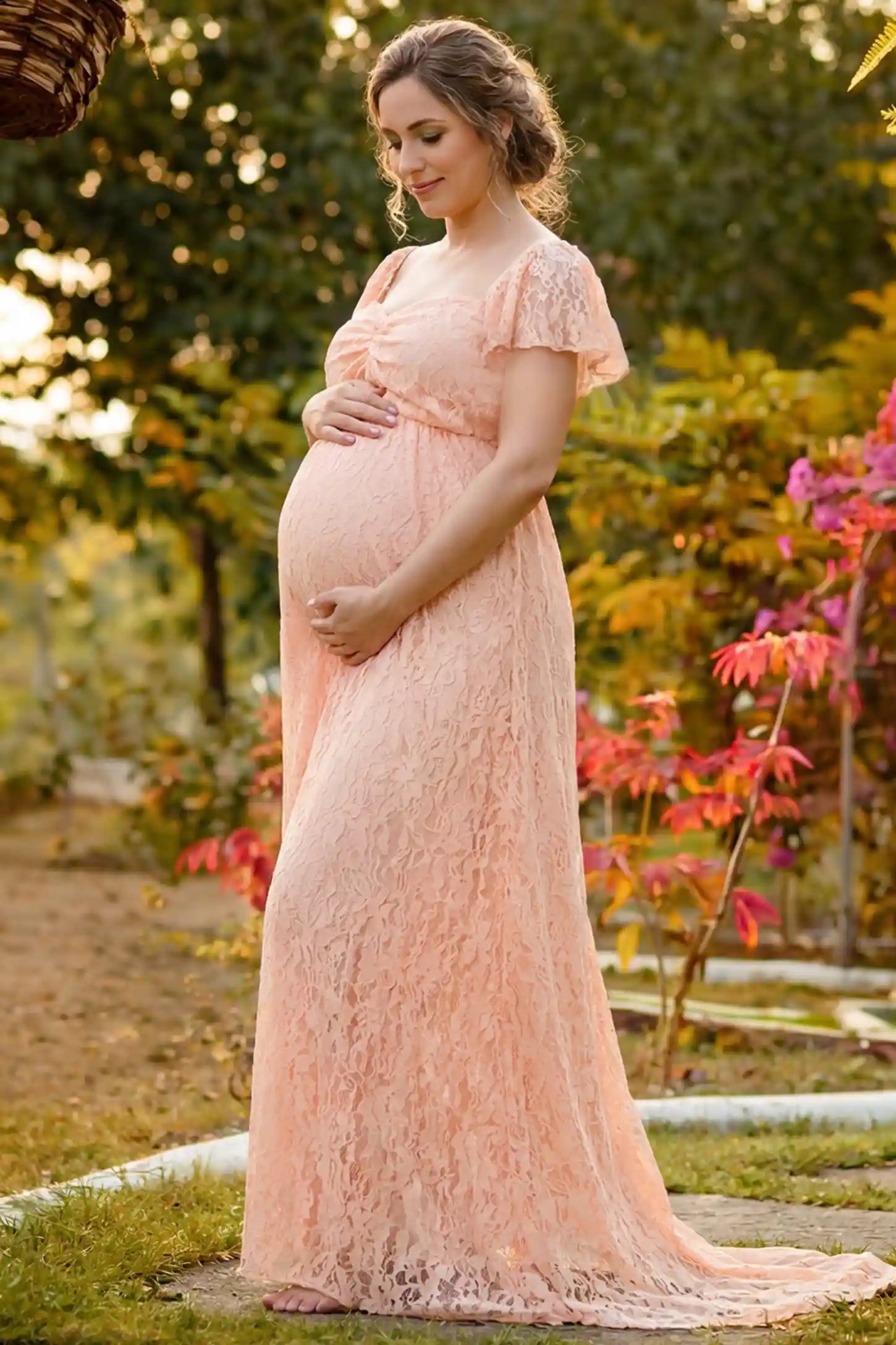 Lace Off Shoulder Maternity Maxi Dress in blush pink featuring a sweetheart neckline with a ruched bust and a full-length skirt, shown on a pregnant woman in a garden, side view.
