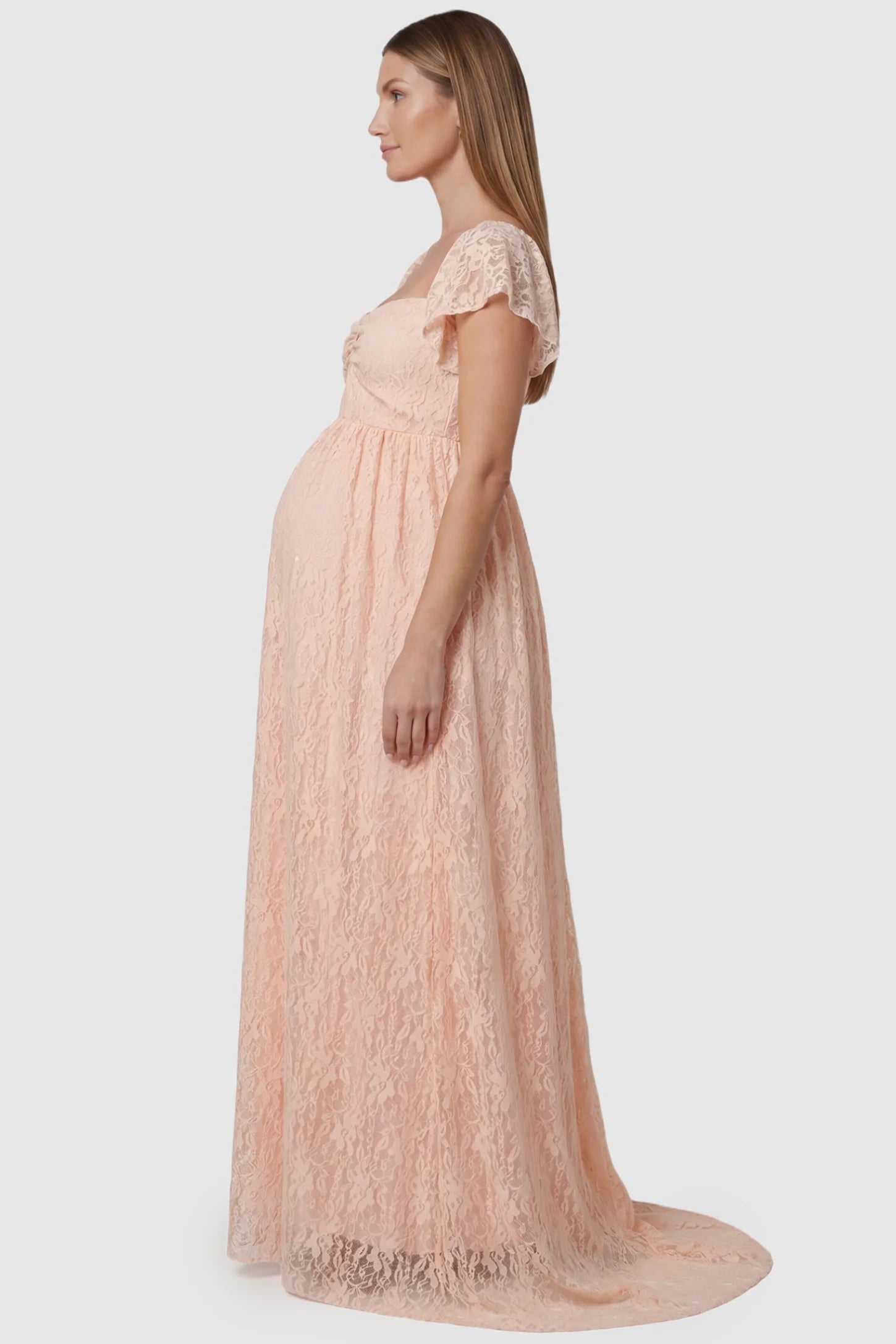 Lace Off Shoulder Maternity Maxi Dress Lace Off Shoulder Maternity Maxi Dress in blush pink featuring a sweetheart neckline with a ruched bust and a full-length skirt, shown on a pregnant model, side view.