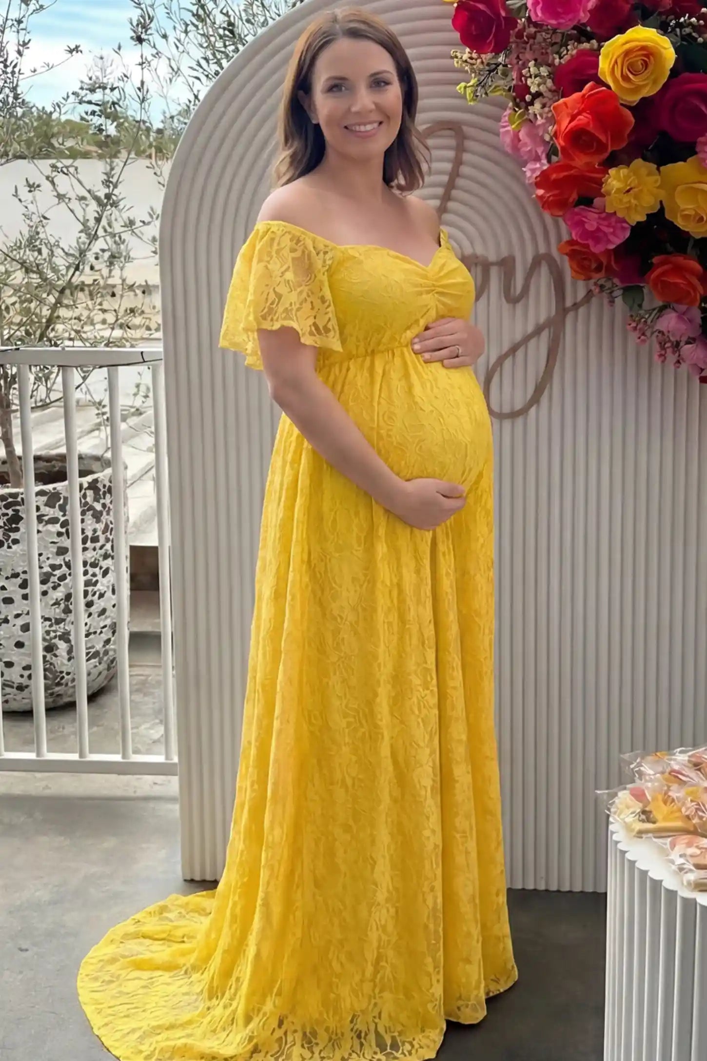 Lace Off Shoulder Maternity Maxi Dress Lace Off Shoulder Maternity Maxi Dress in ginger yellow featuring a sweetheart neckline with a ruched bust and a full-length skirt, shown on a pregnant woman at a baby shower, front view.