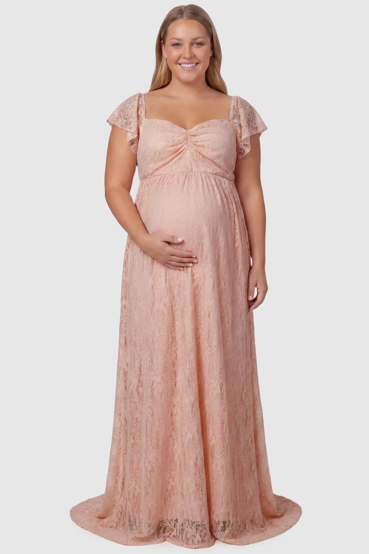 Lace Off Shoulder Maternity Maxi Dress Lace Off Shoulder Maternity Maxi Dress in pink featuring a sweetheart neckline with a ruched bust and a full-length skirt, shown on a plus size pregnant model, front view.